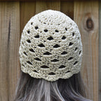 Beige crochet hat worn by a person with long hair against a wooden background.