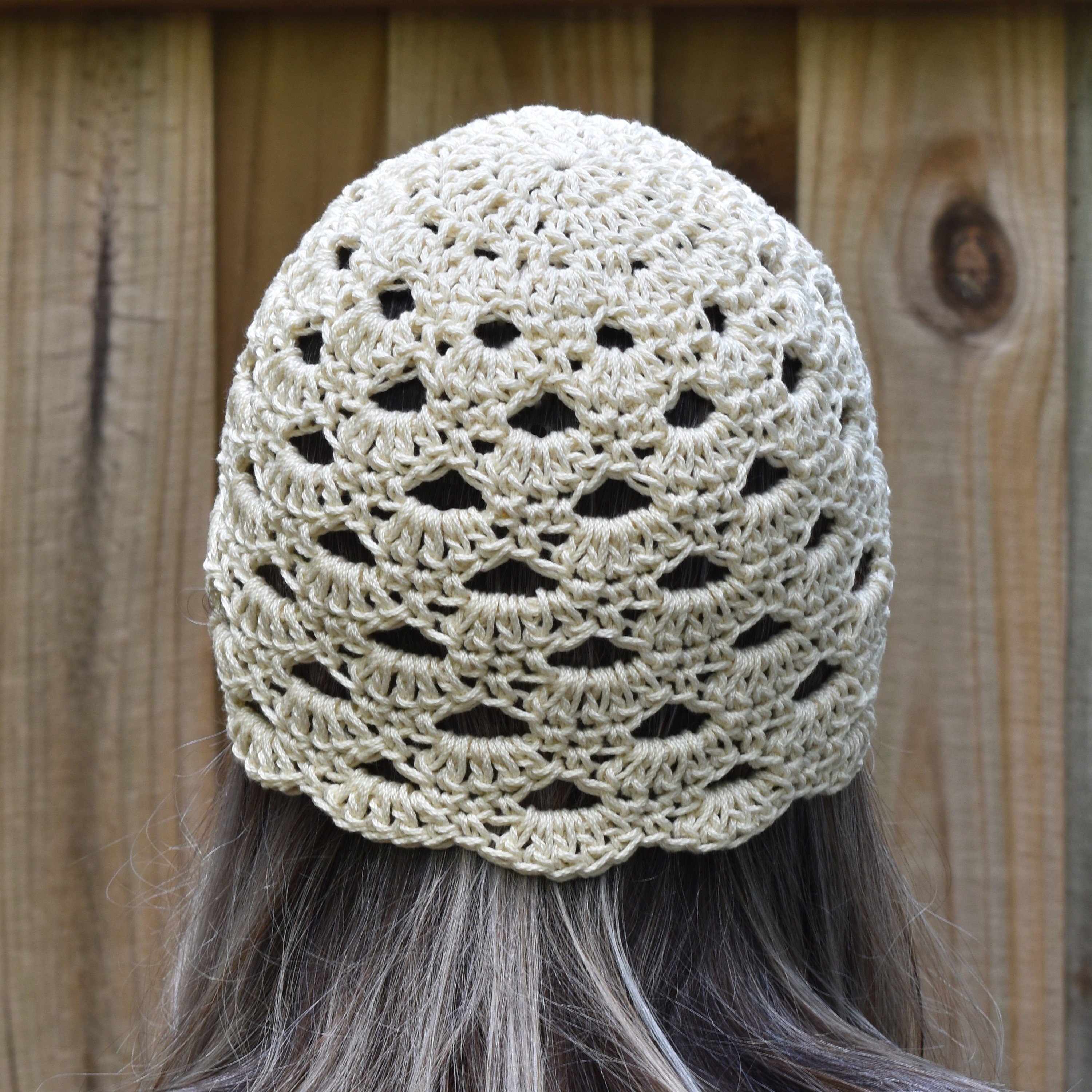 Beige crochet hat worn by a person with long hair against a wooden background.