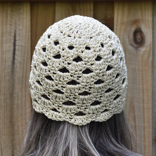 Beige crochet hat worn by a person with long hair against a wooden background.