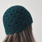A teal knitted beanie worn by a person with long hair against a neutral background.