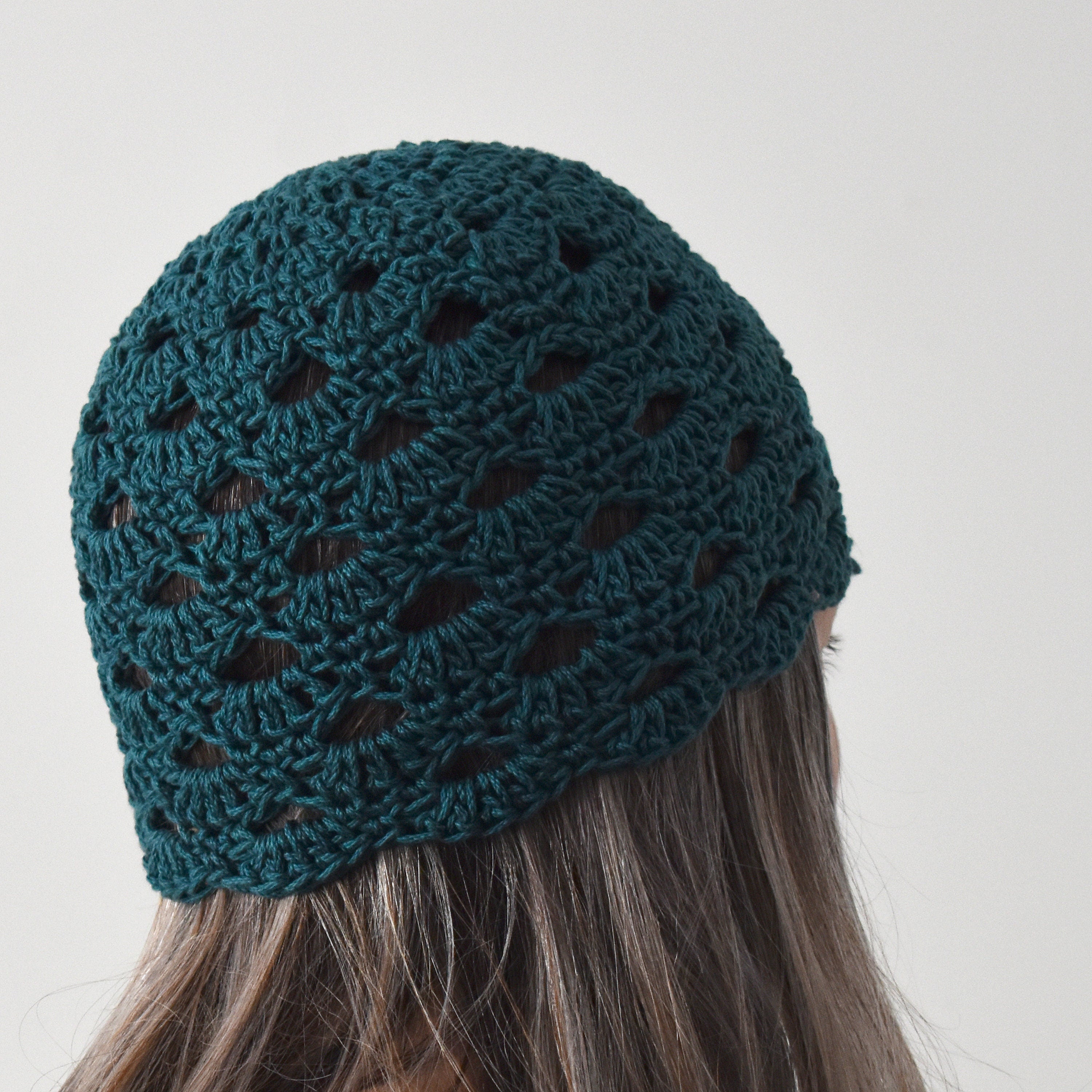 A teal knitted beanie worn by a person with long hair against a neutral background.