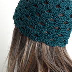 Teal knitted beanie on a person with long hair against a white background.
