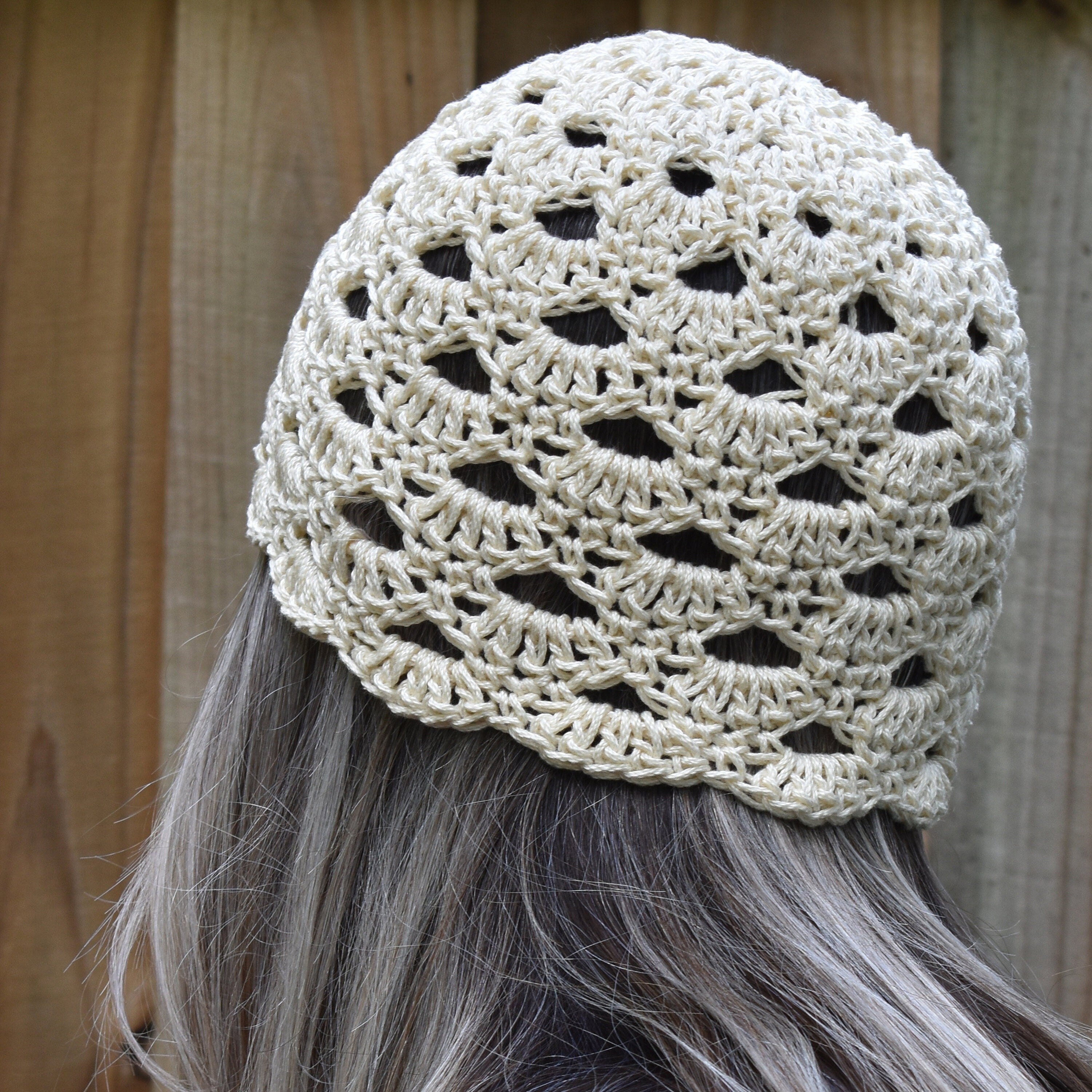 Crocheted beige beanie worn by a person with gray hair against a wooden background.