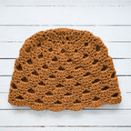 Amber orange crocheted hat on a white wooden surface.