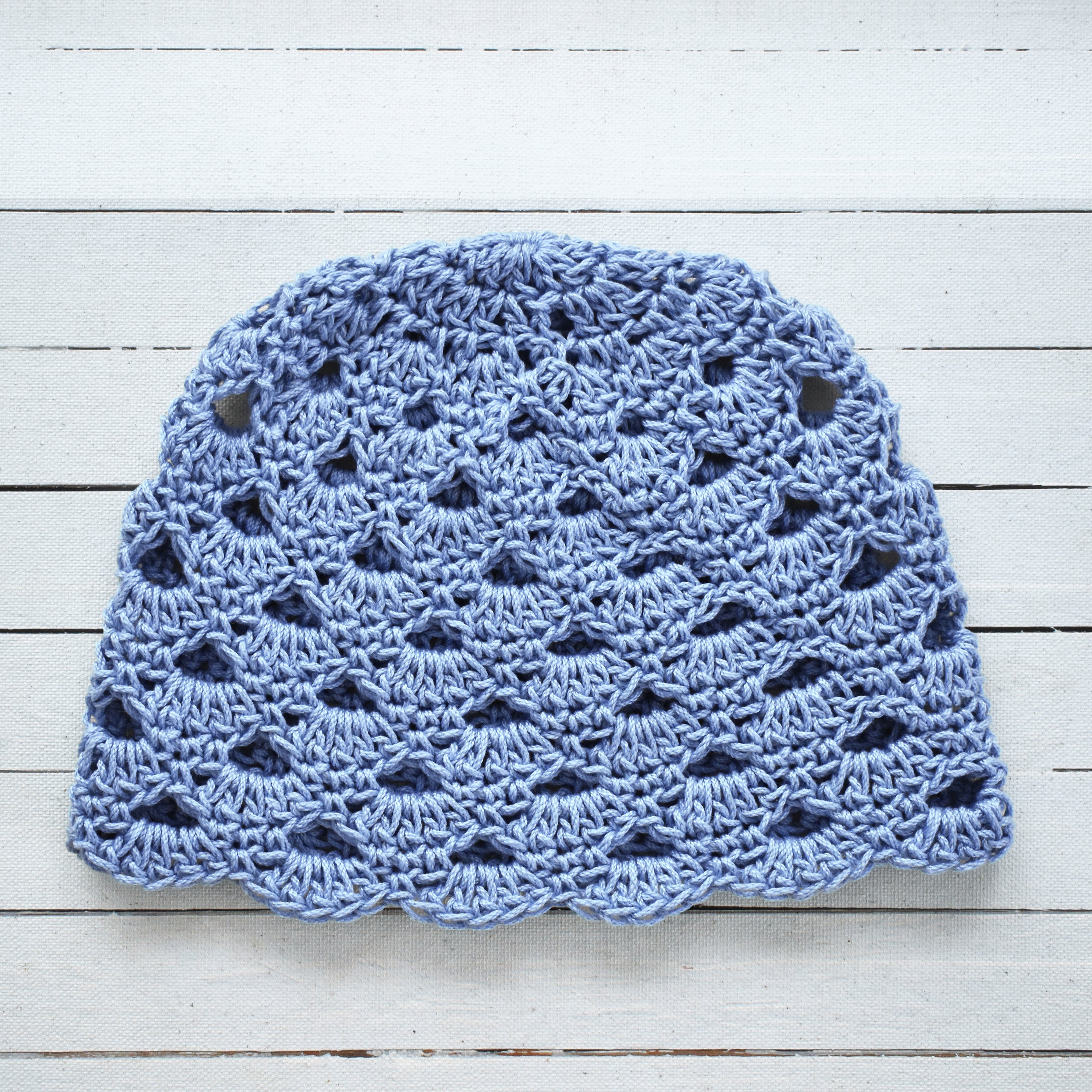 Baby blue crocheted hat on a light wooden surface.