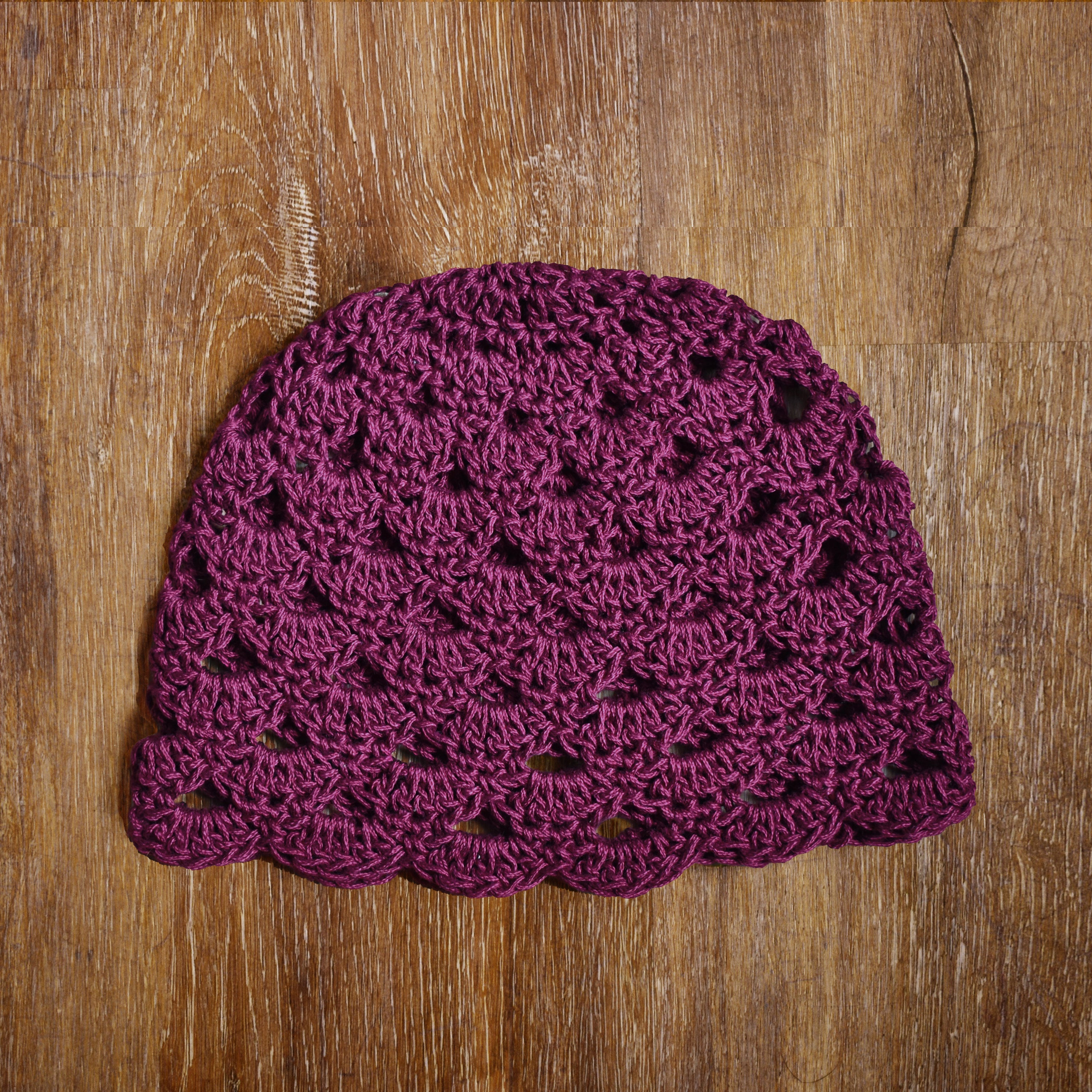 Reddish purple crocheted hat on a wooden surface.