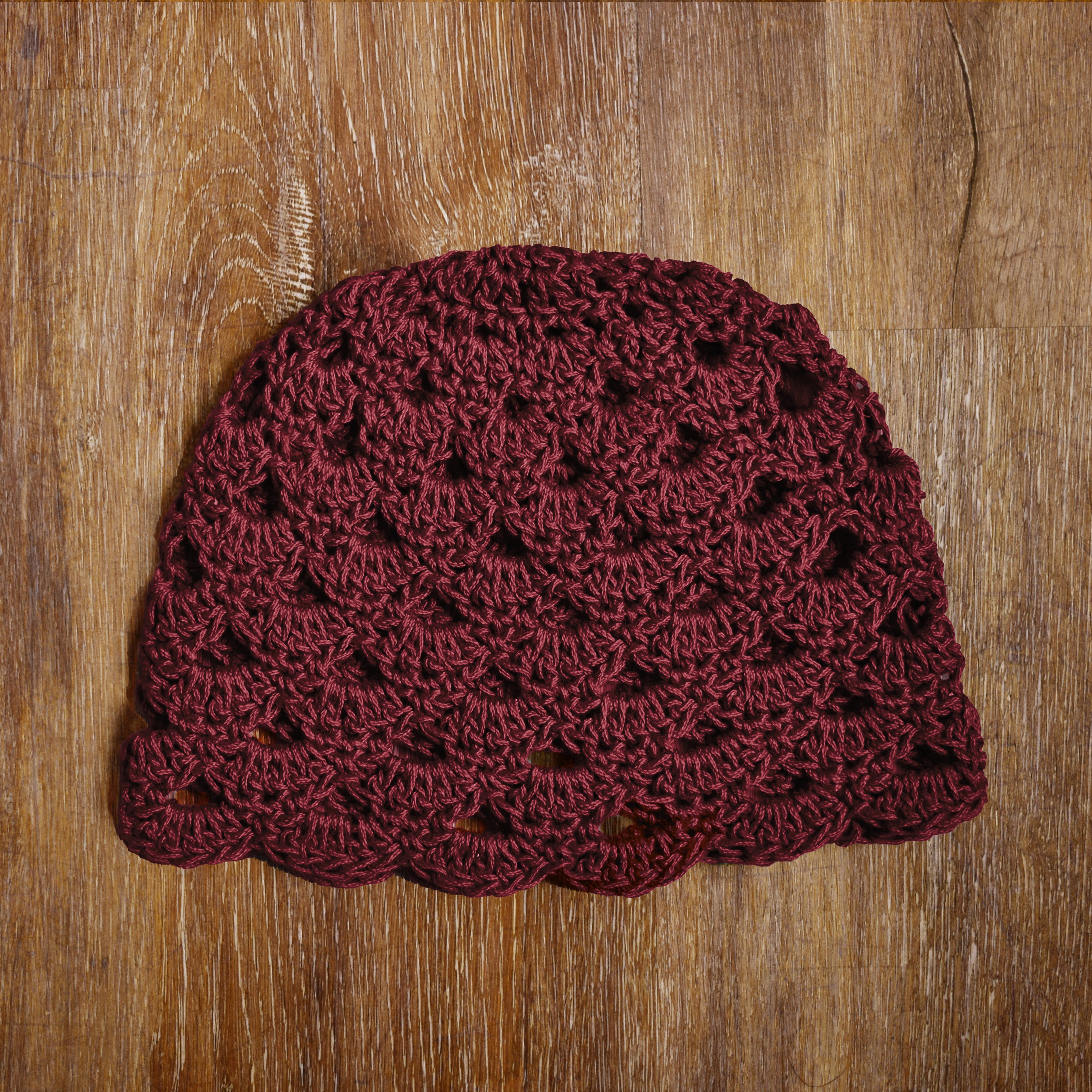 Maroon crocheted beanie on a wooden surface.