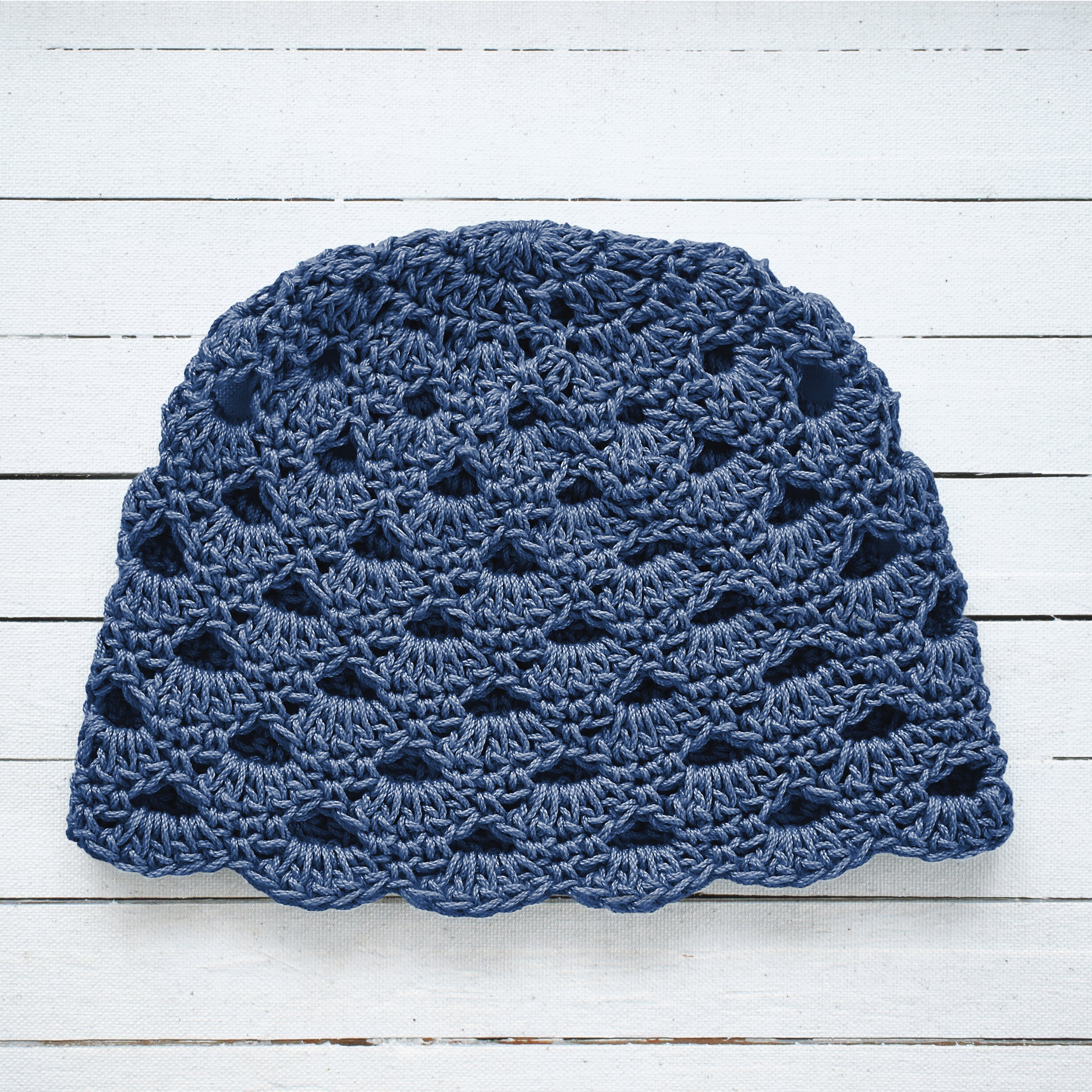Gray-blue crochet hat on a white wooden surface.