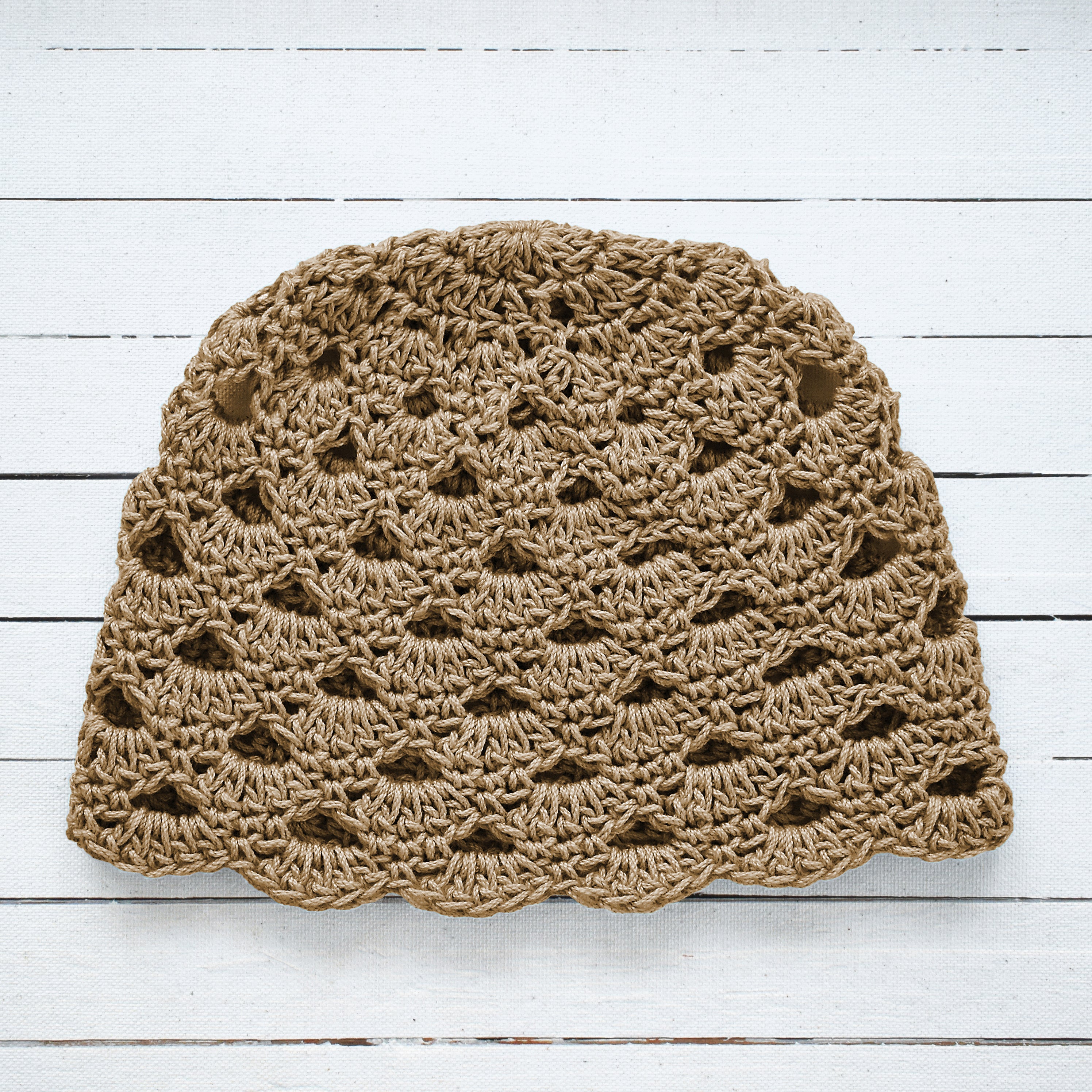 Tan crochet hat on a white wooden surface.