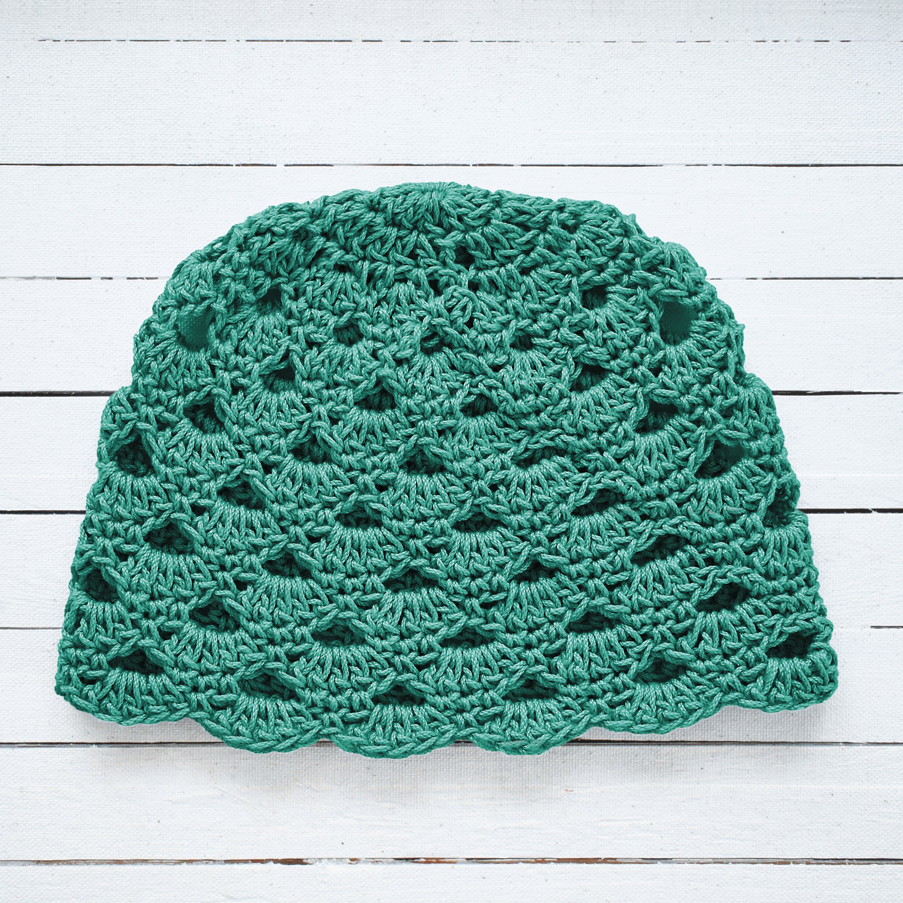 Light teal crocheted beanie on a white wooden surface.