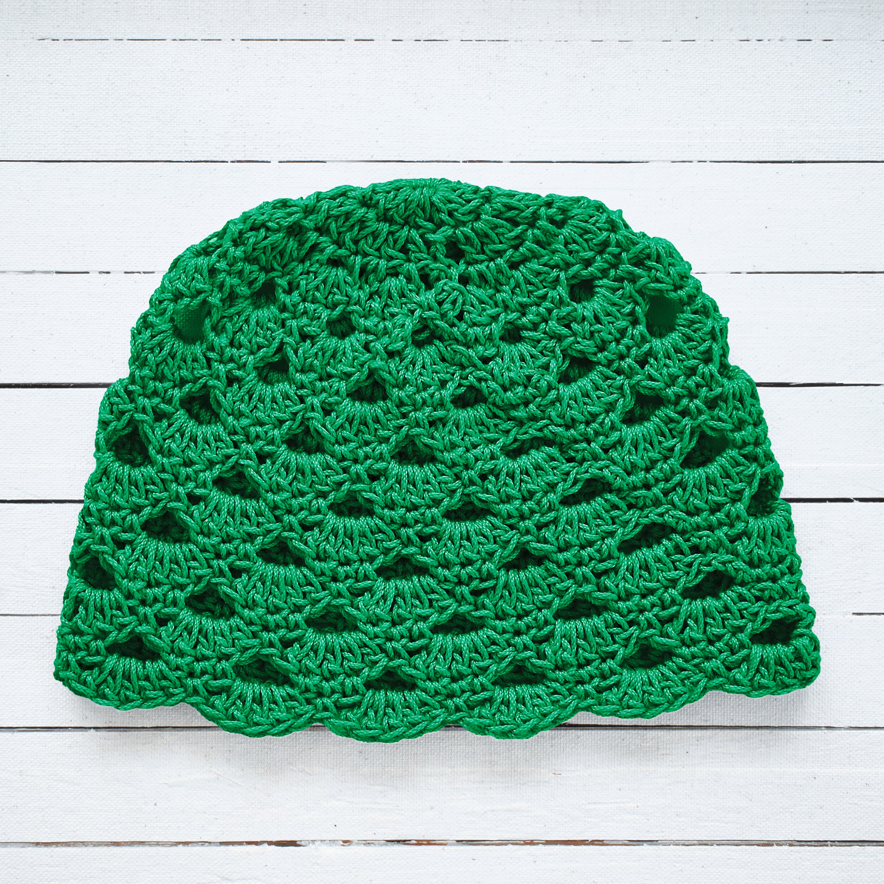 Green crochet beanie on a white wooden surface.