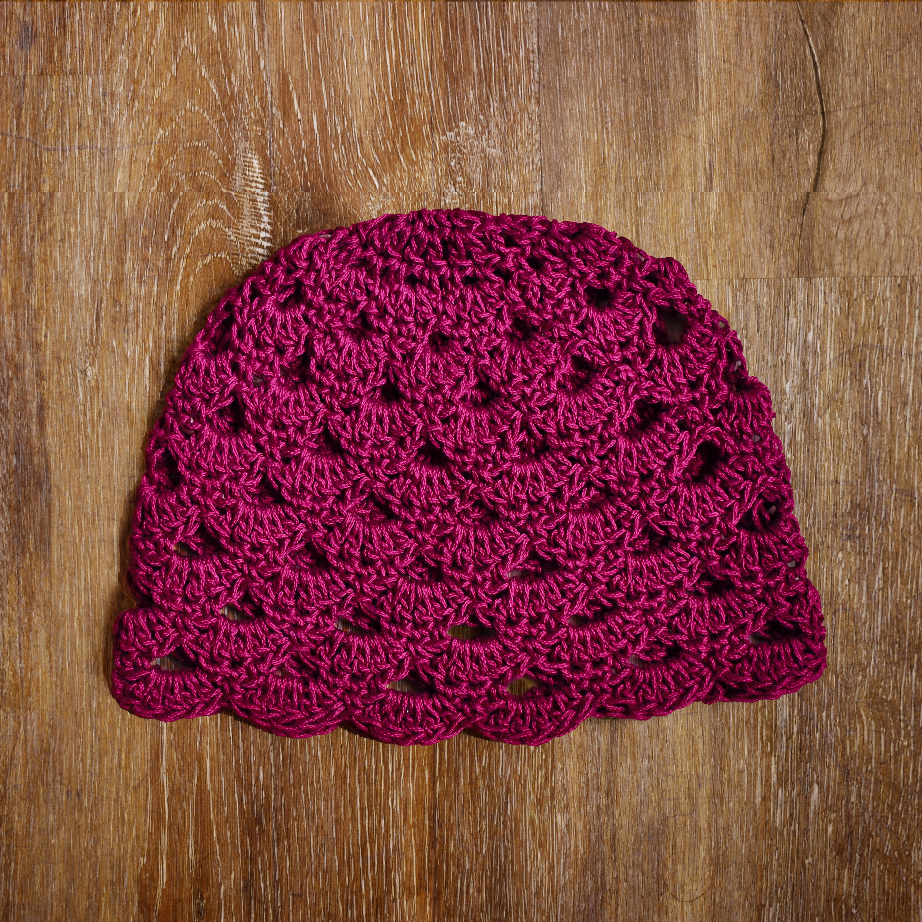 Magenta pink crocheted hat on a wooden surface.