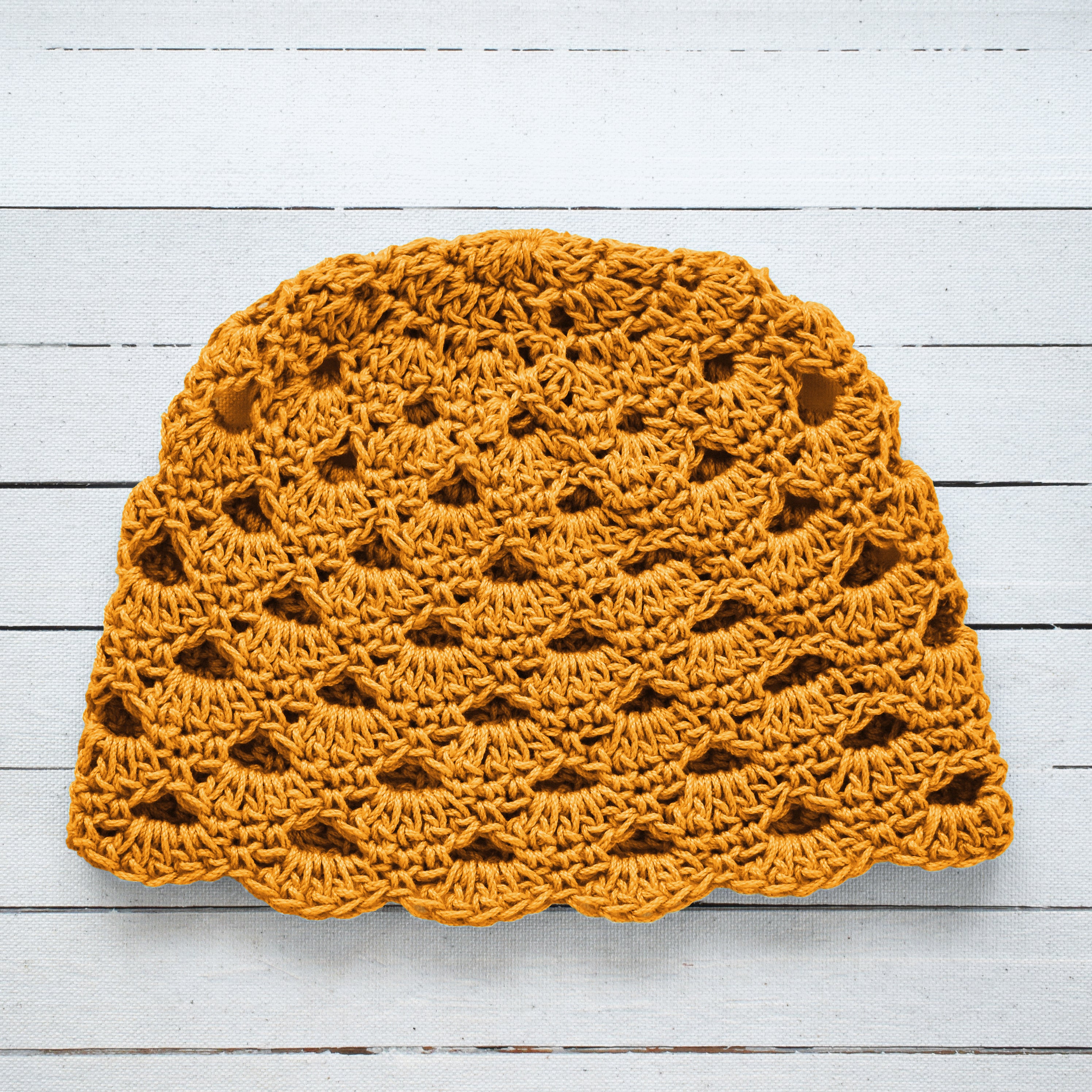 Yellow crochet beanie on a white wooden surface.