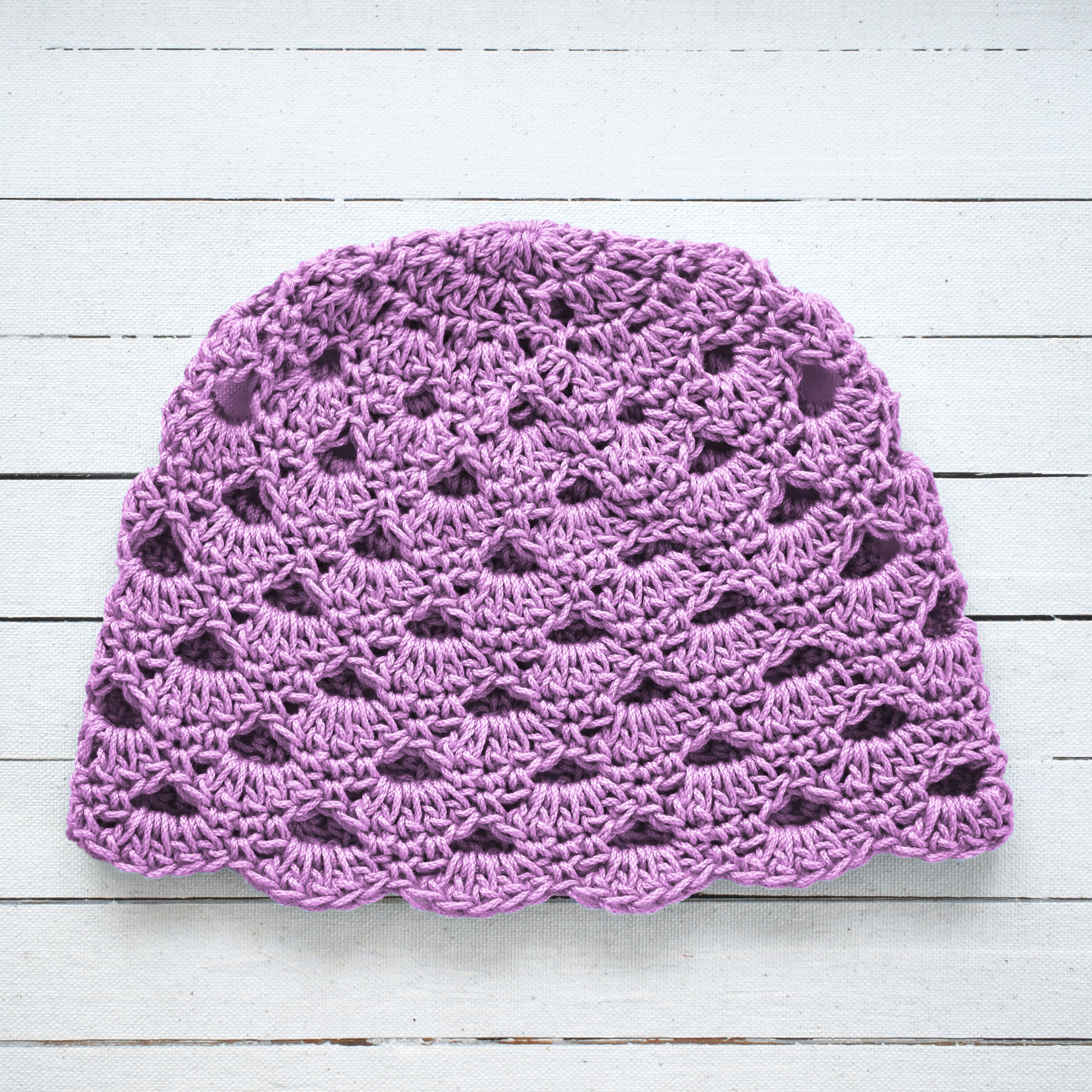 Light purple crocheted hat on a light wooden surface.