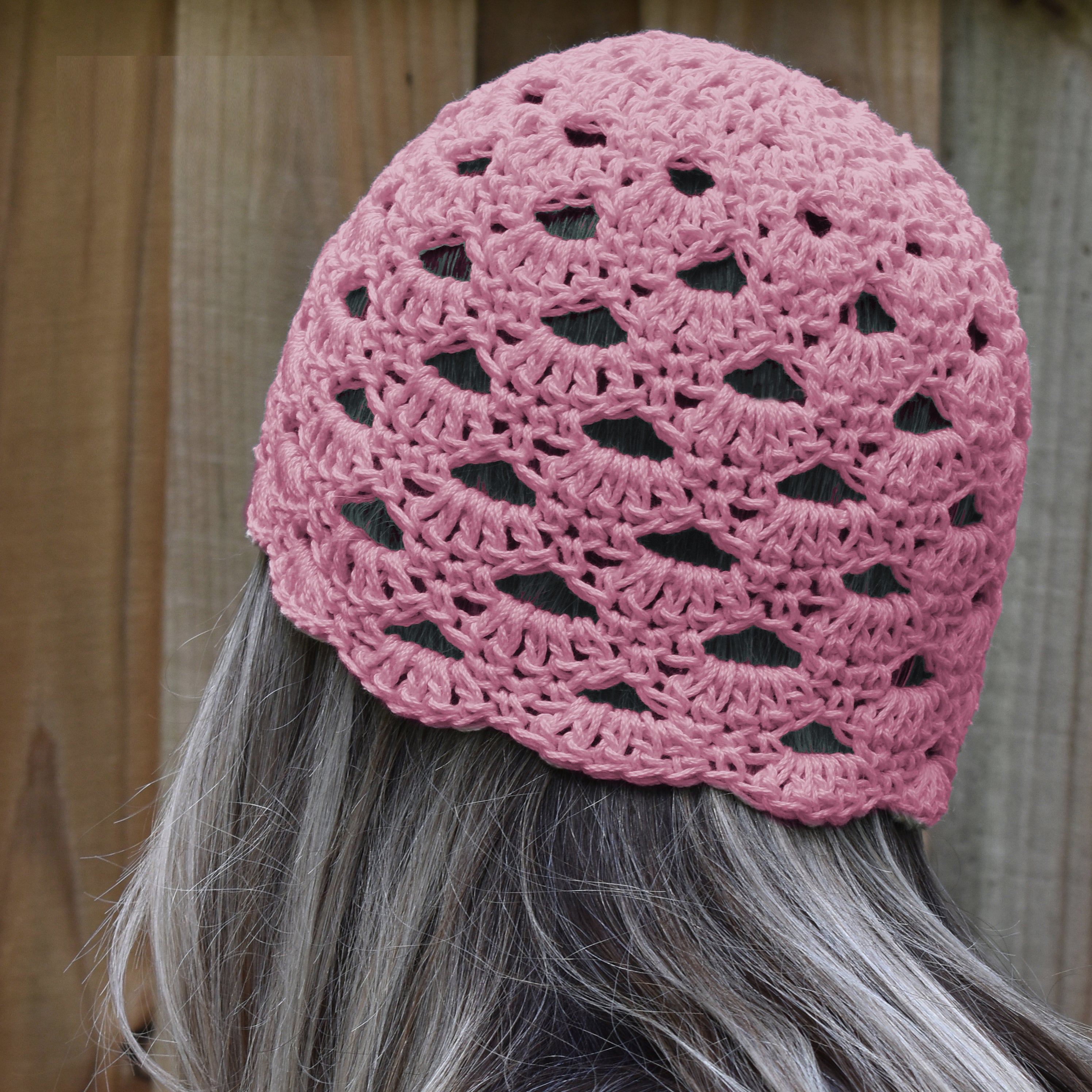 Pink crocheted beanie worn by a person with gray hair against a wooden background.