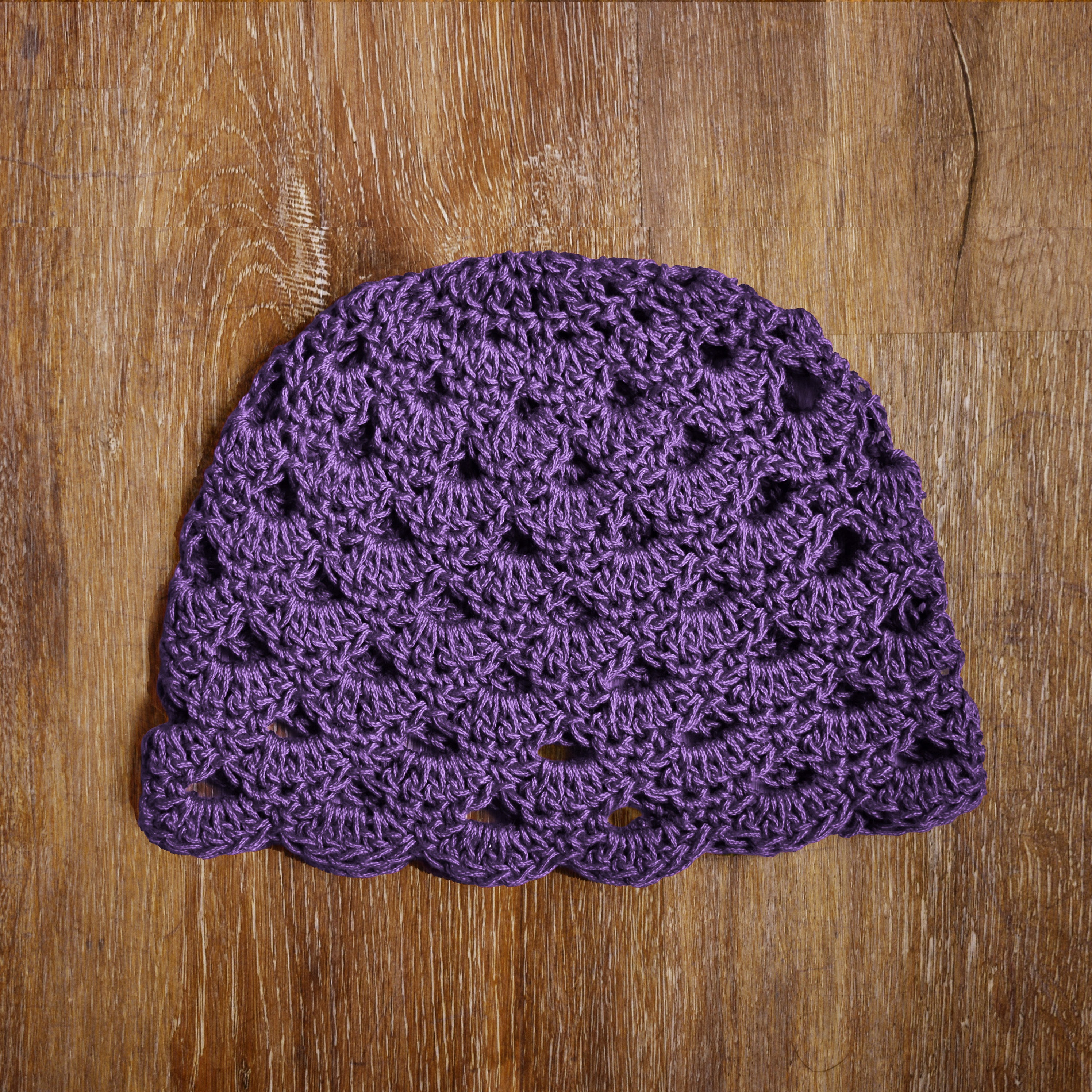 Purple crocheted hat on a wooden surface.
