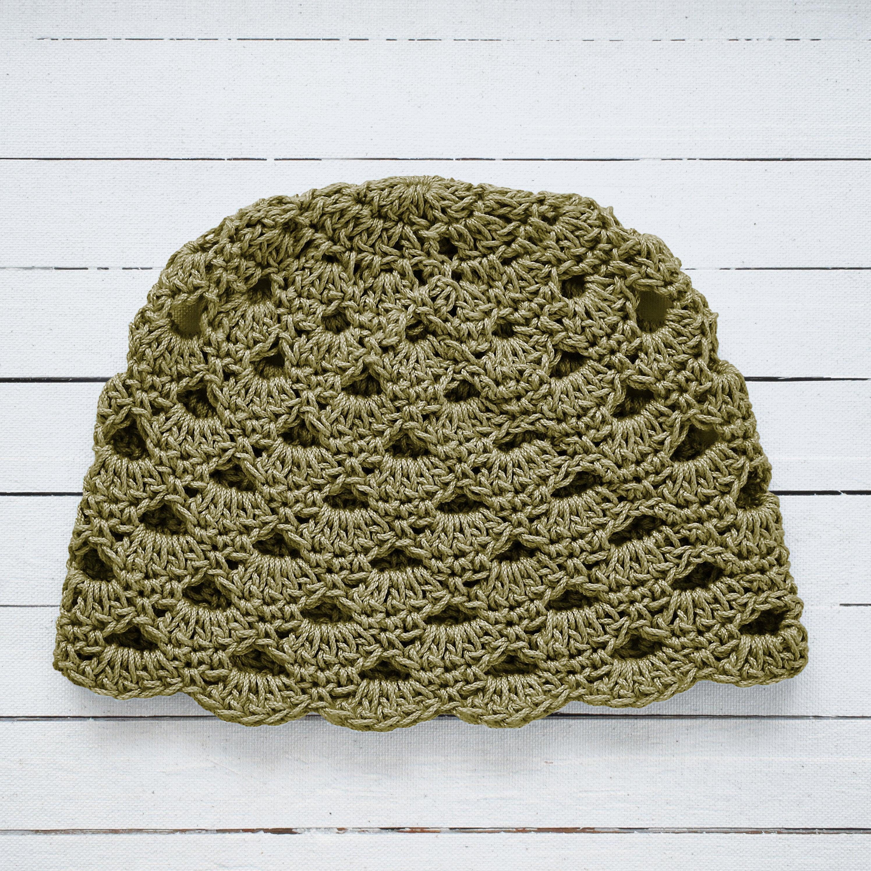 Sage green crochet hat on a white wooden surface.