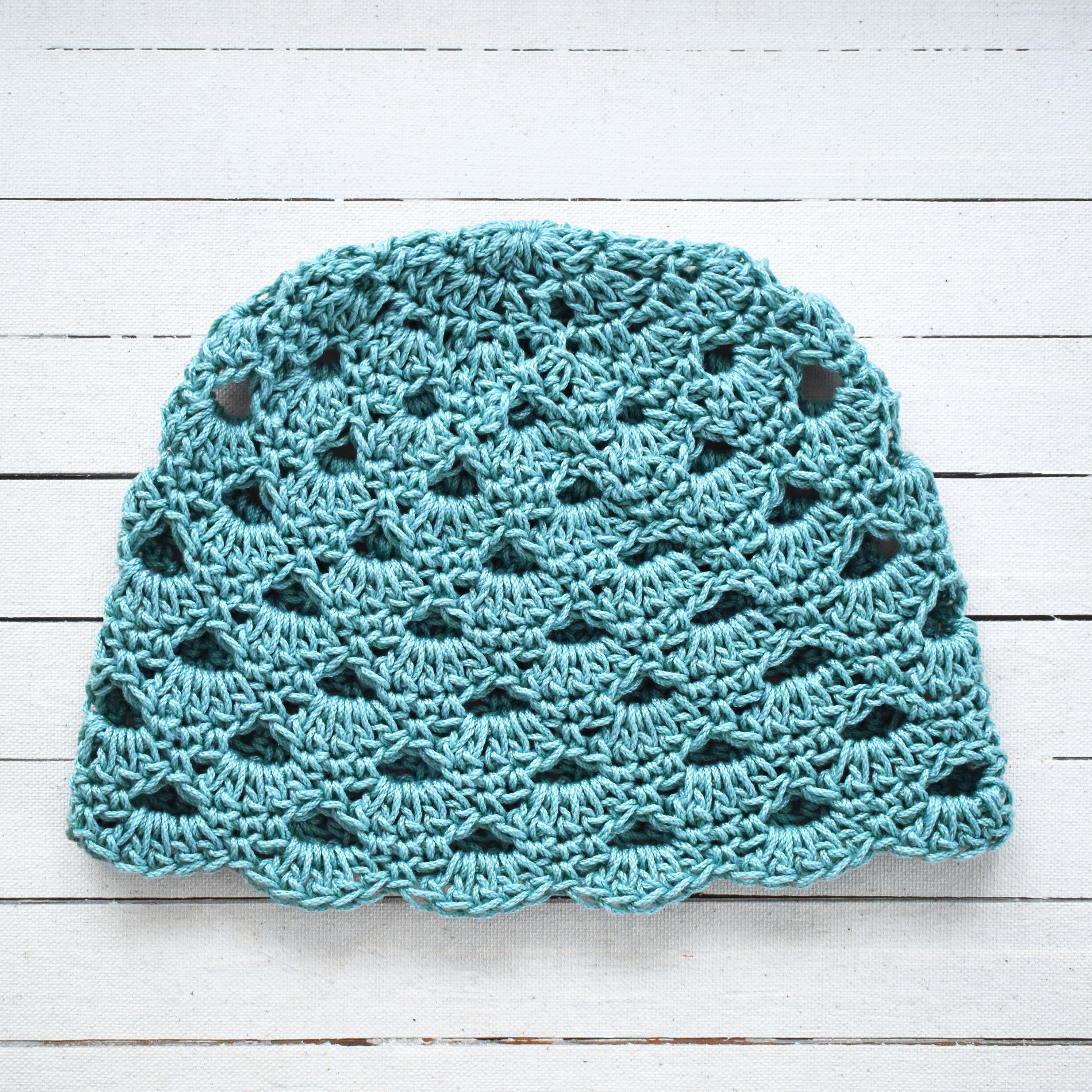 Light blue crochet hat on a white wooden surface.