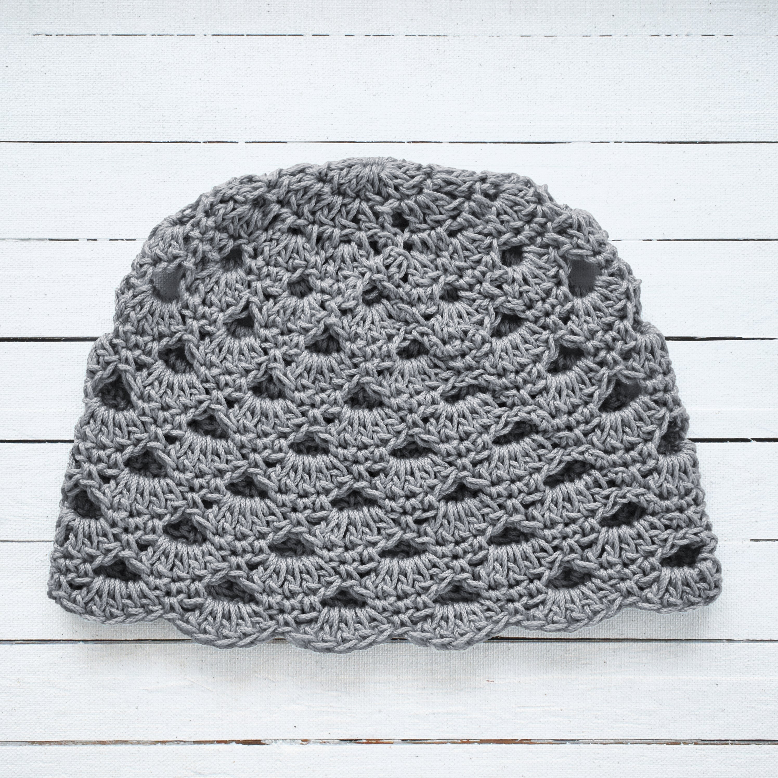 Gray crochet beanie on a white wooden surface.