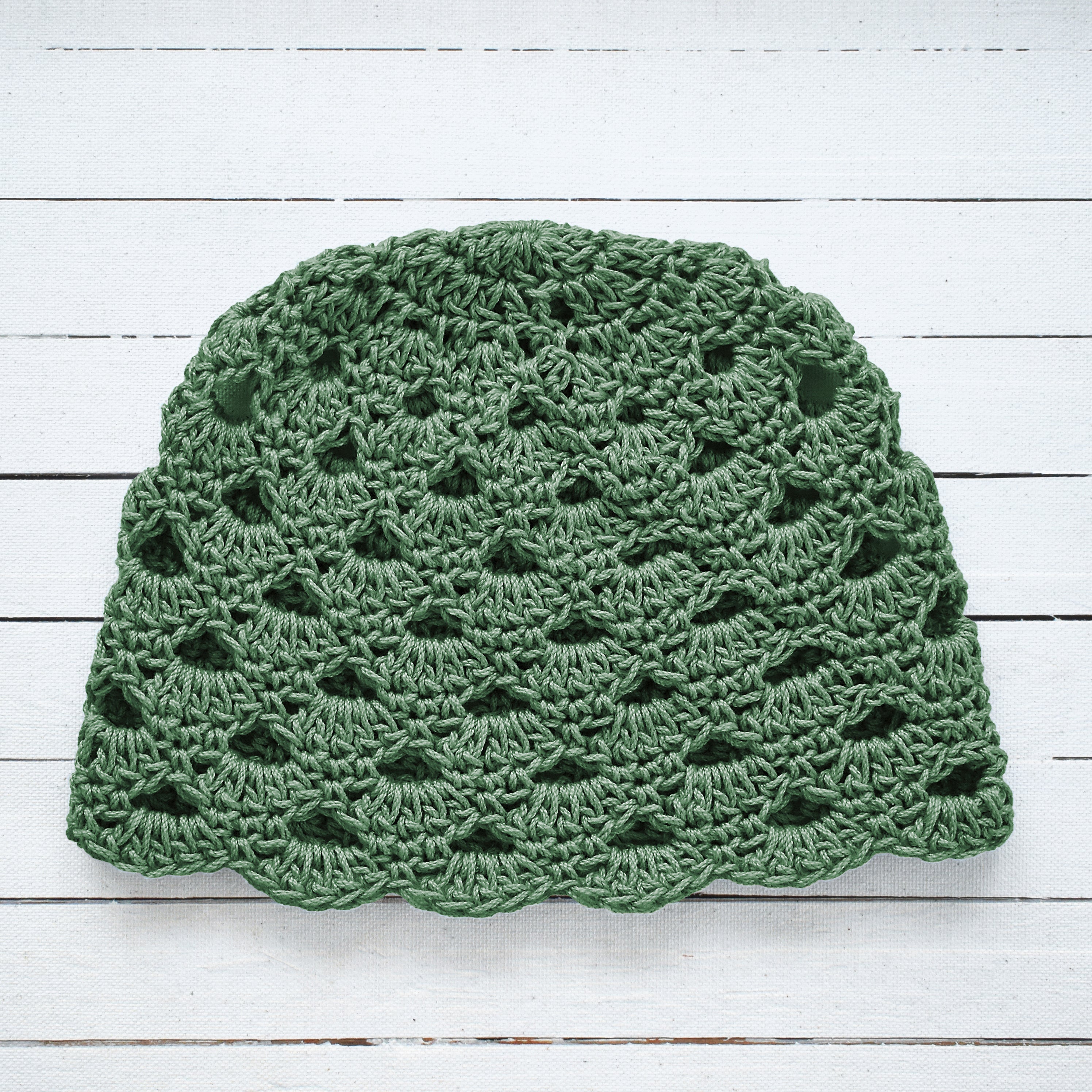 Earthy green crochet hat on a white wooden surface.