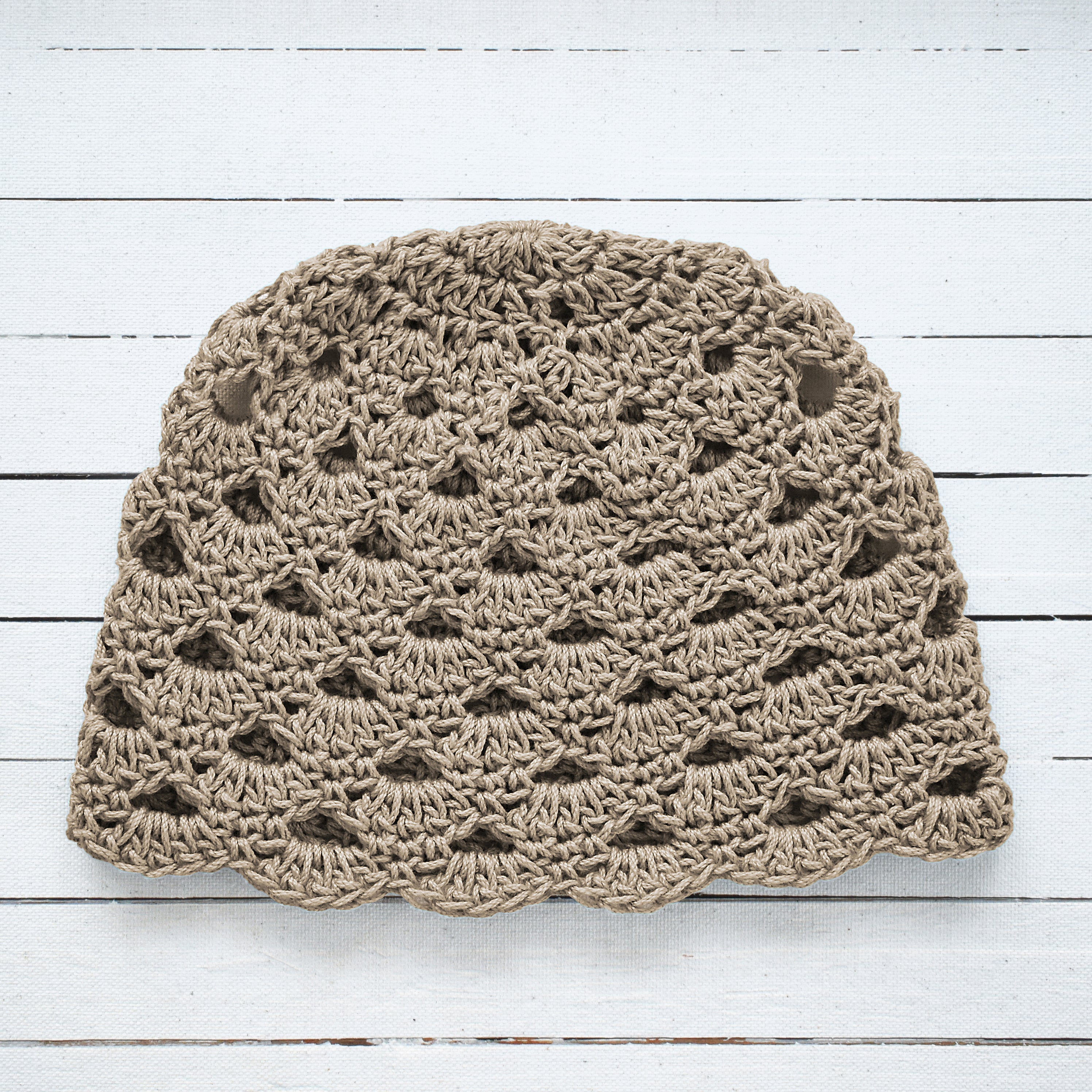 Crocheted beanie in taupe color on a white wooden background.