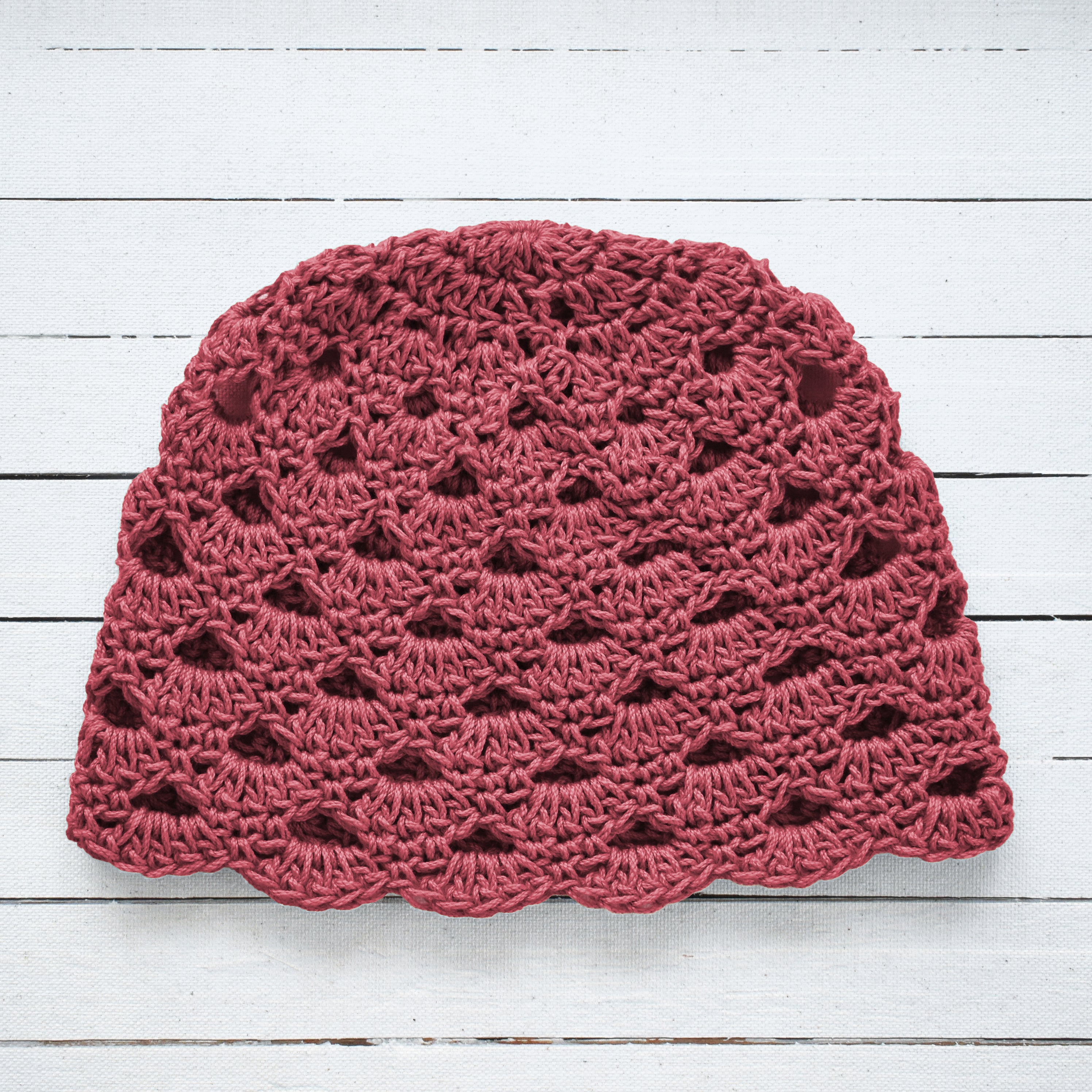 Earthy pink handmade crochet hat on a white wooden surface.