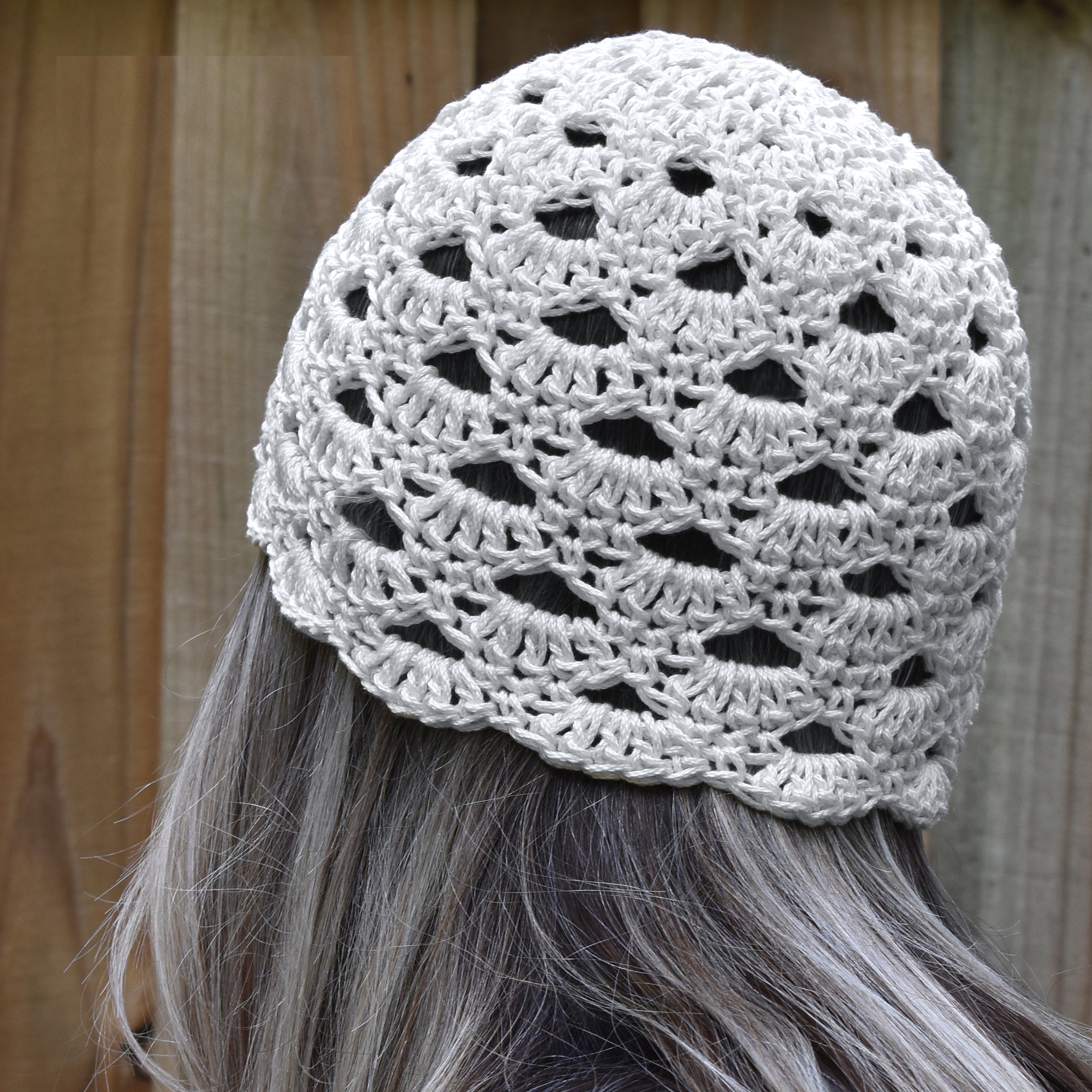 White crochet hat worn by a person with long hair against a wooden background.