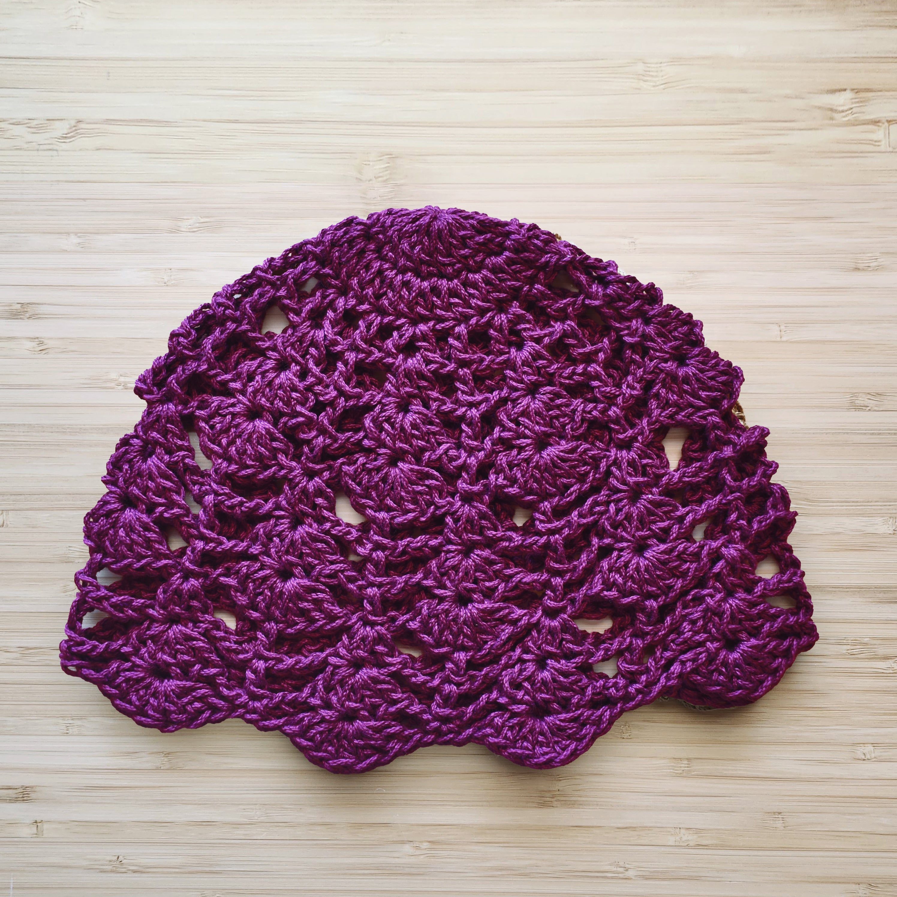 Dark purple crocheted hat on a wooden surface.