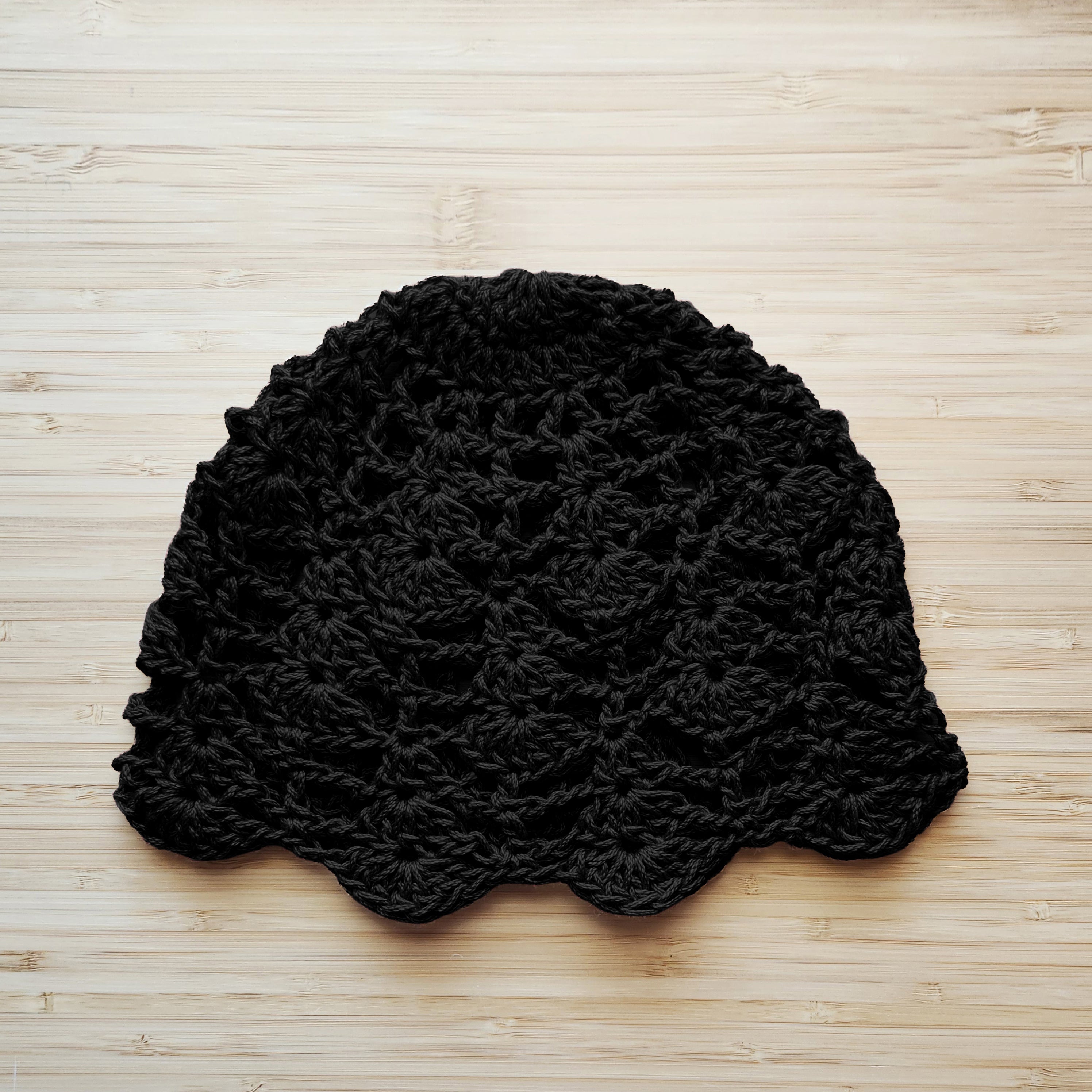 Black crocheted floral lace hat on a light wood surface.