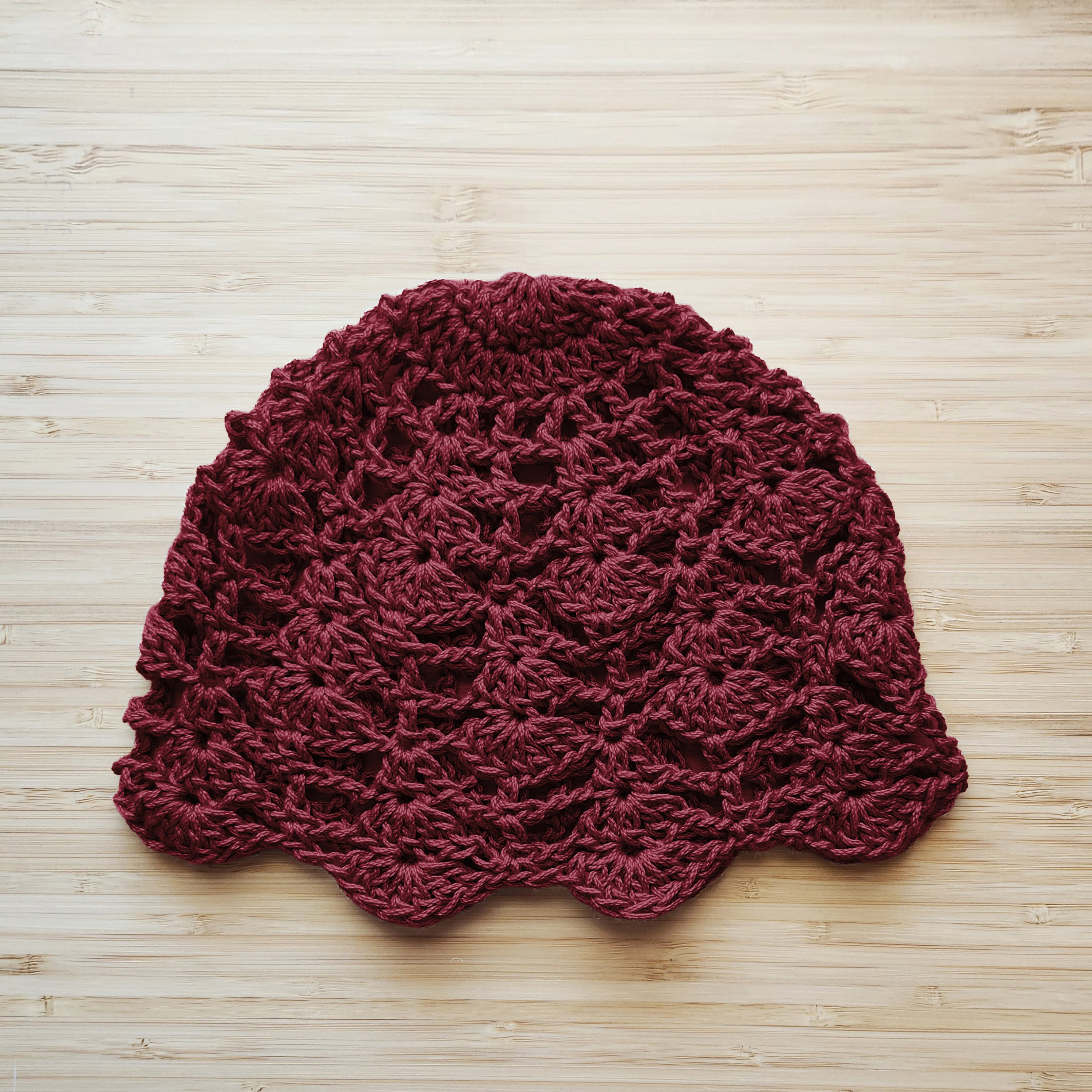 Maroon crocheted hat with a blooming flower design on a wooden surface.