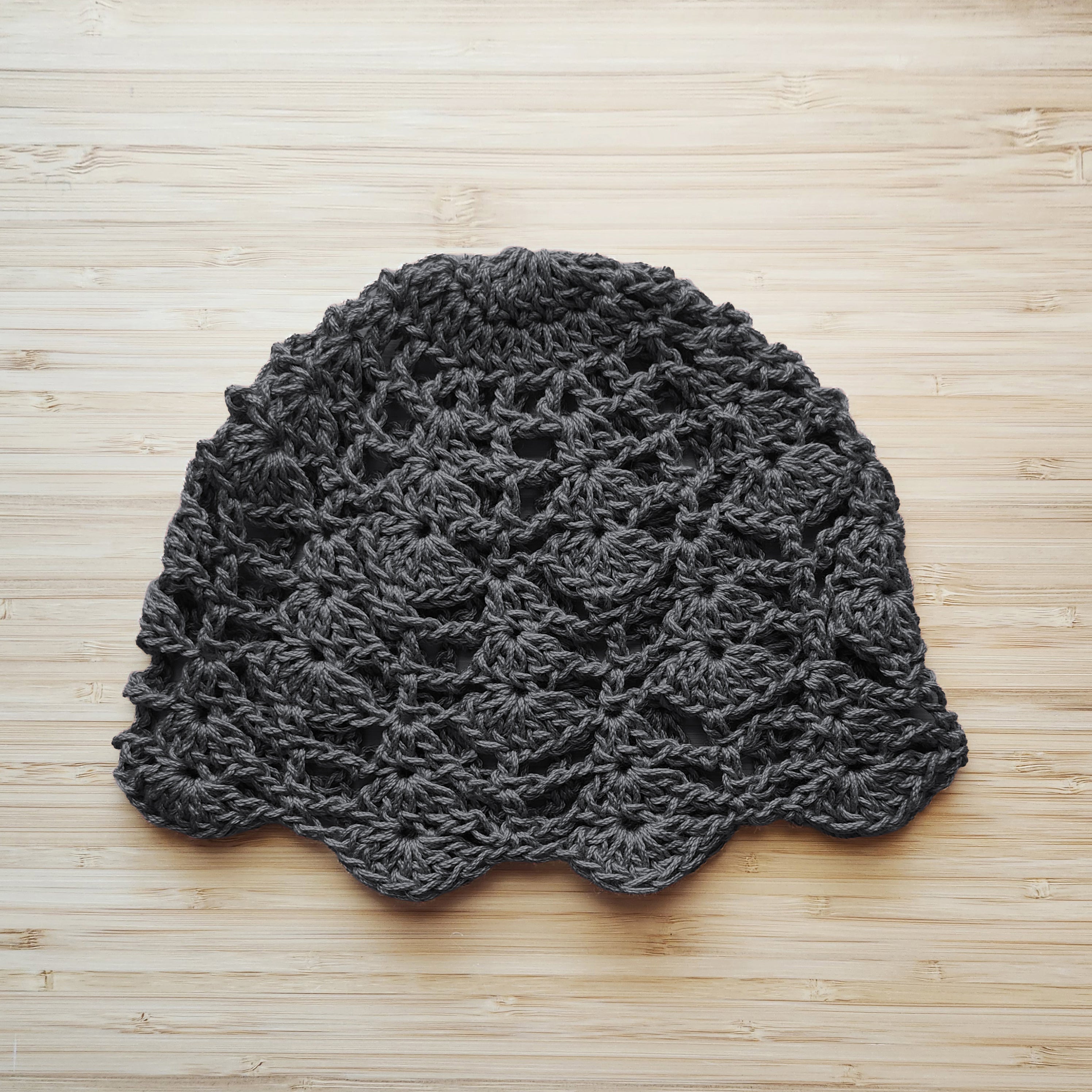Dark gray crochet lace hat on a wooden surface.