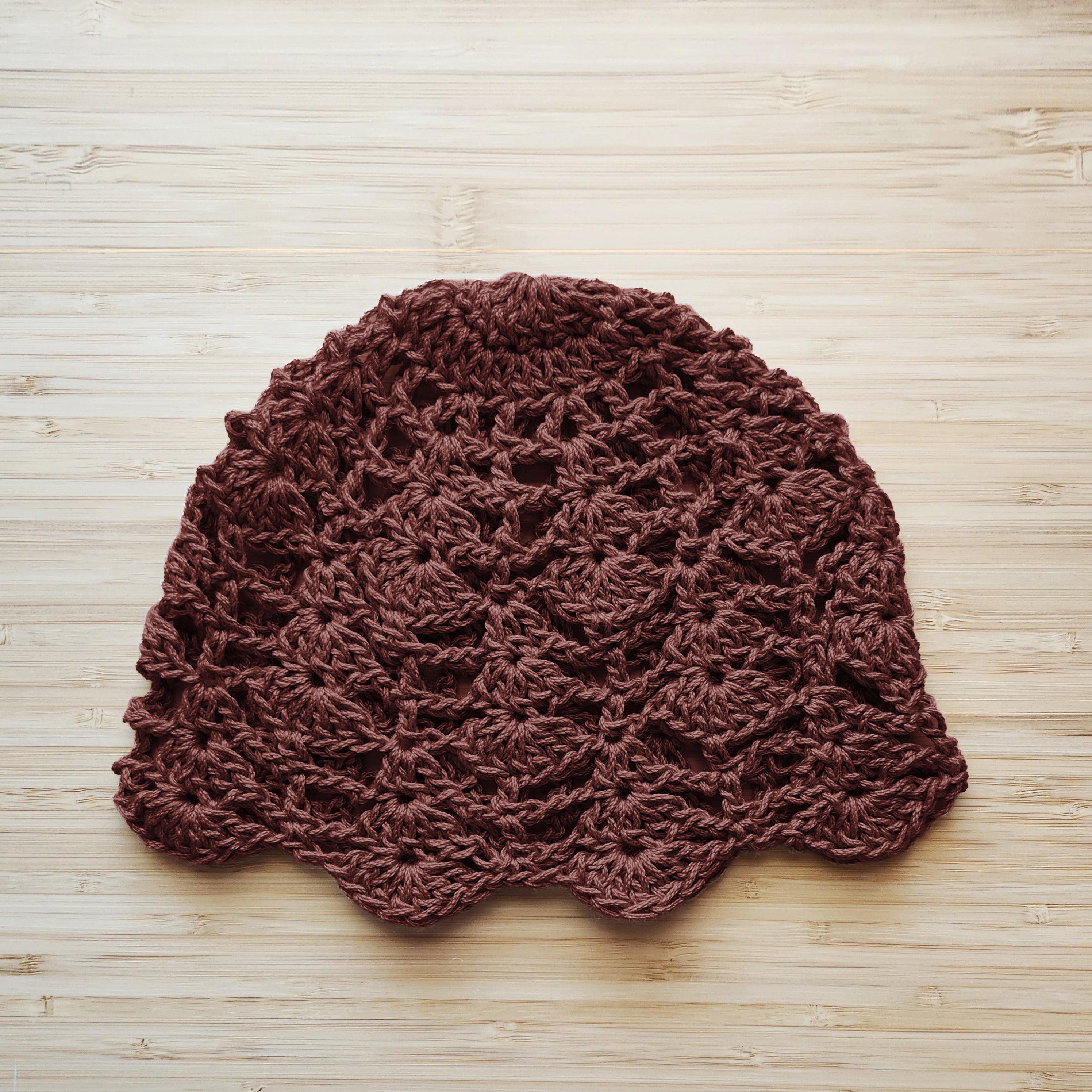 Brown knitted lace hat on a wooden surface.