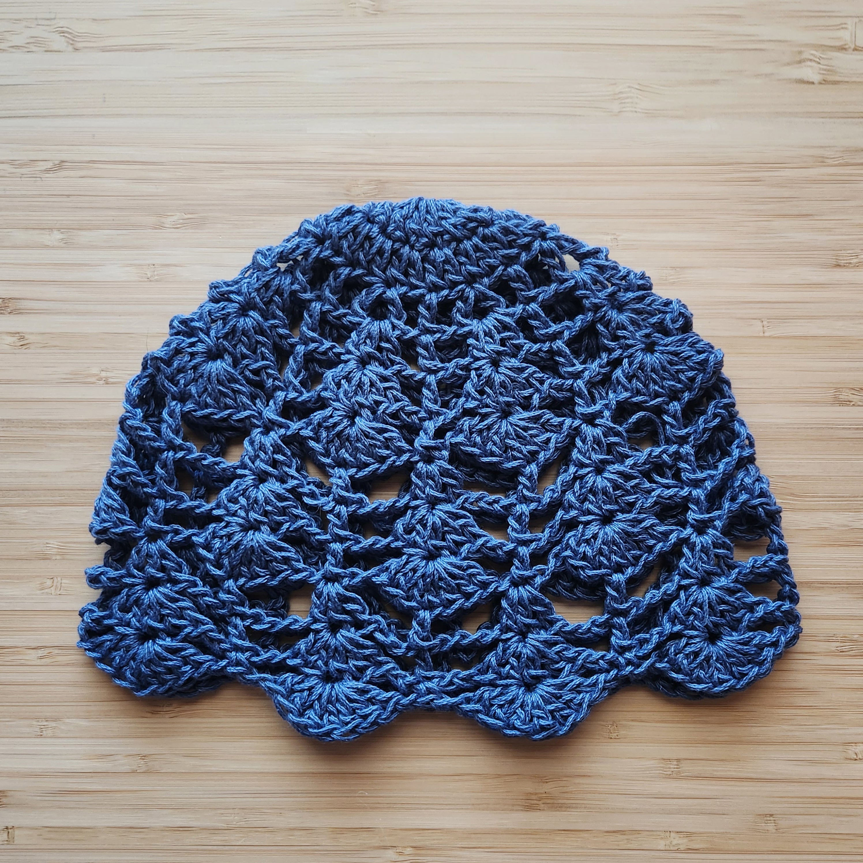 Gray-blue crocheted lace cap on a wooden surface.