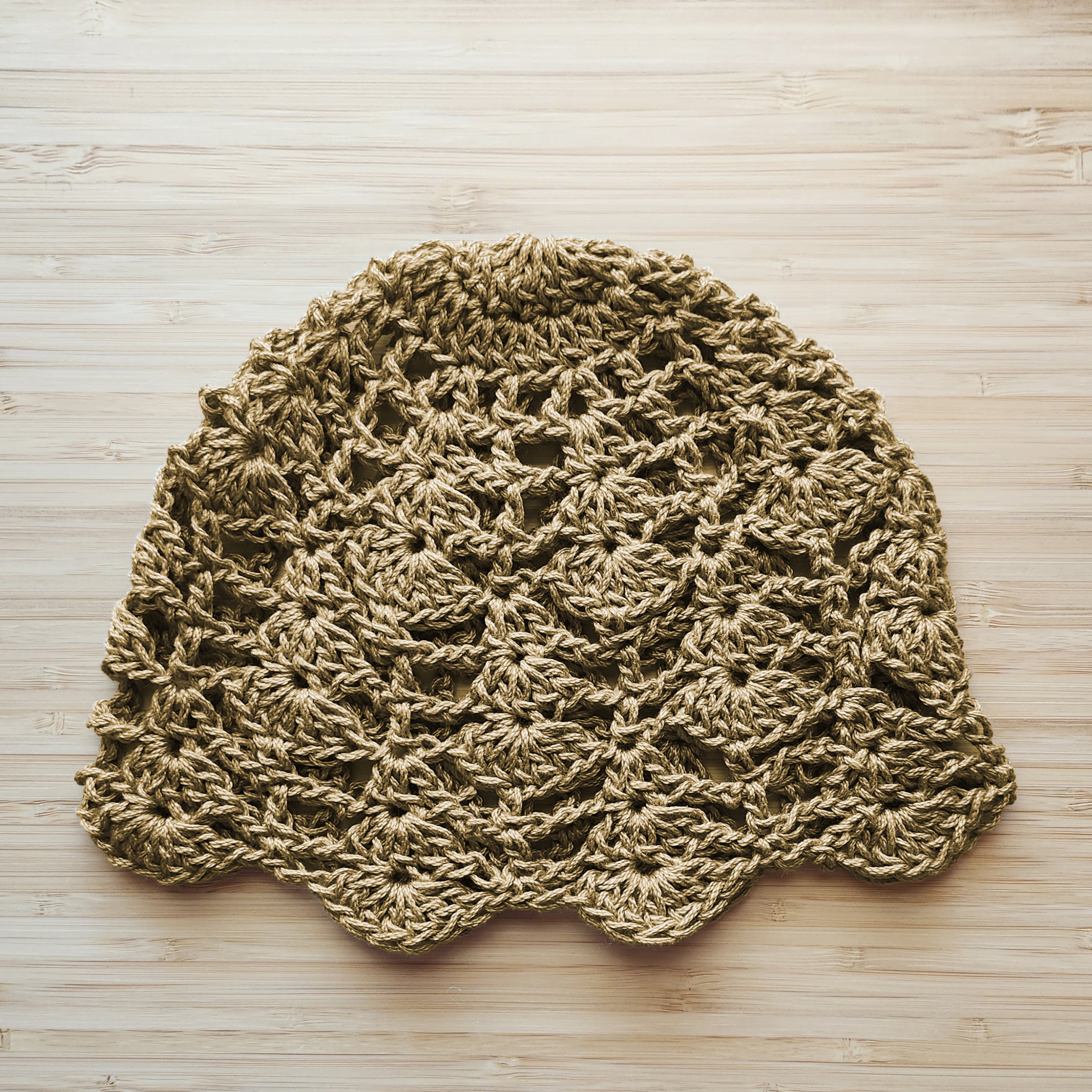 Tan knitted lace hat on a wooden surface.