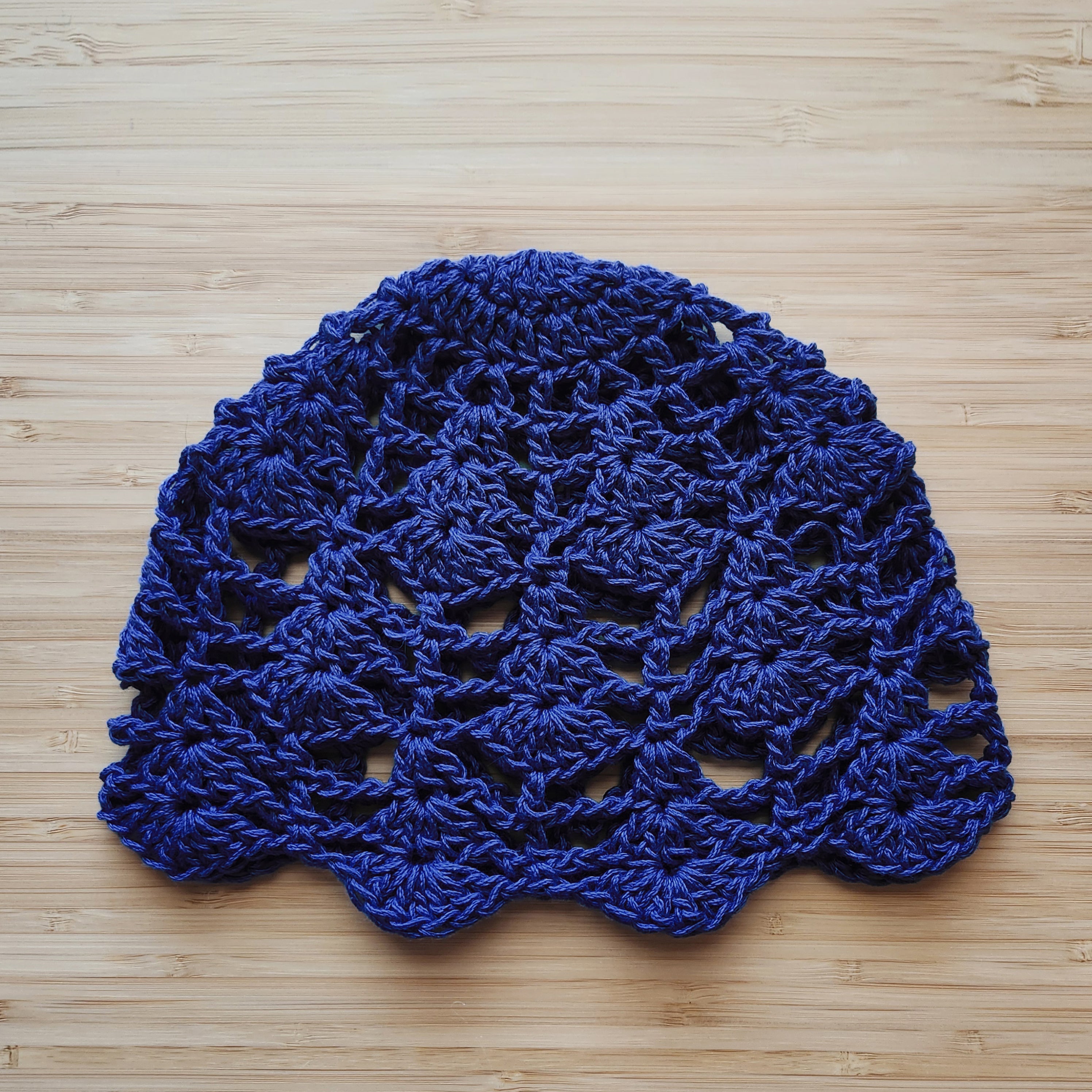 Blue crocheted hat with a flower design on a wooden surface.