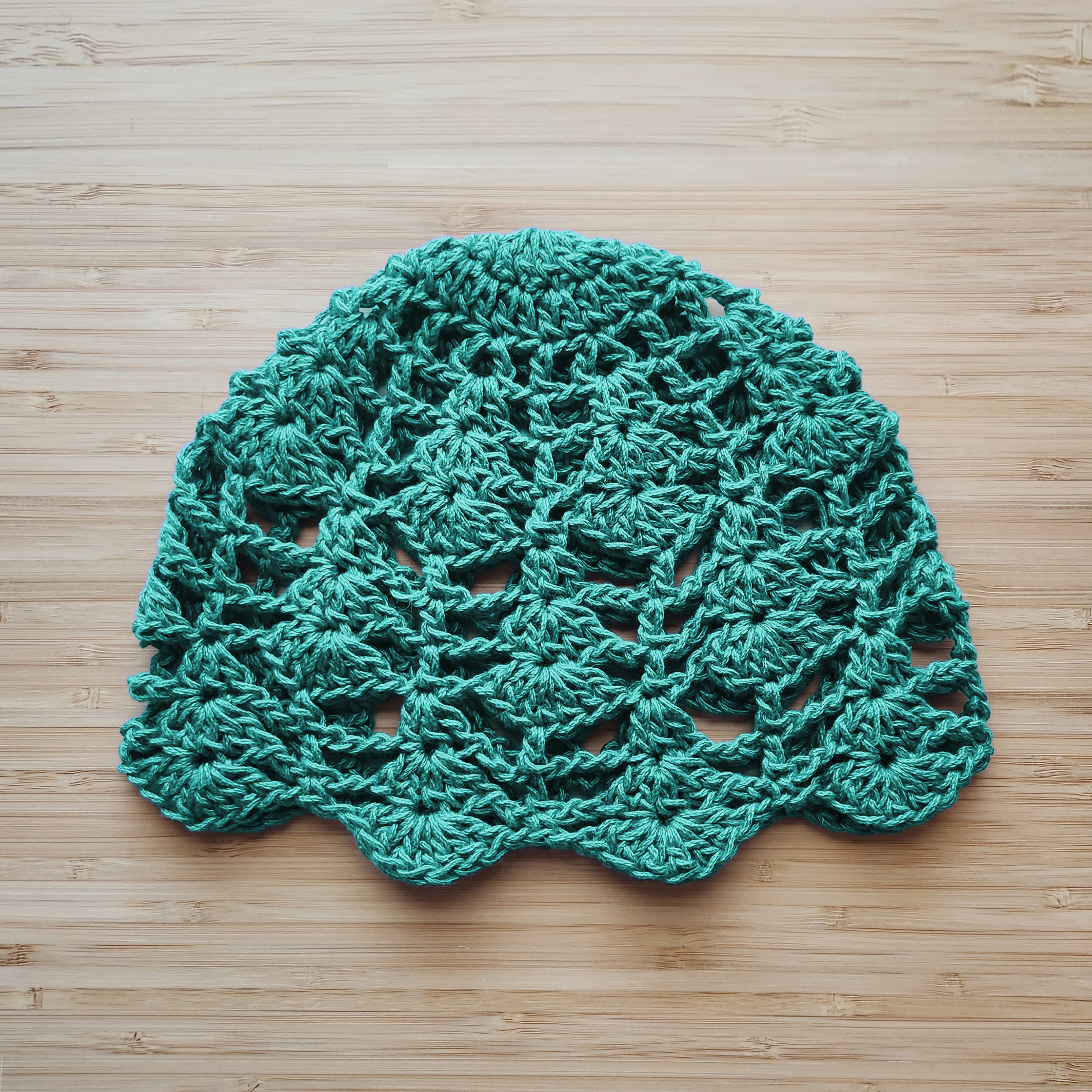 Light teal crocheted lace hat on a wooden surface.