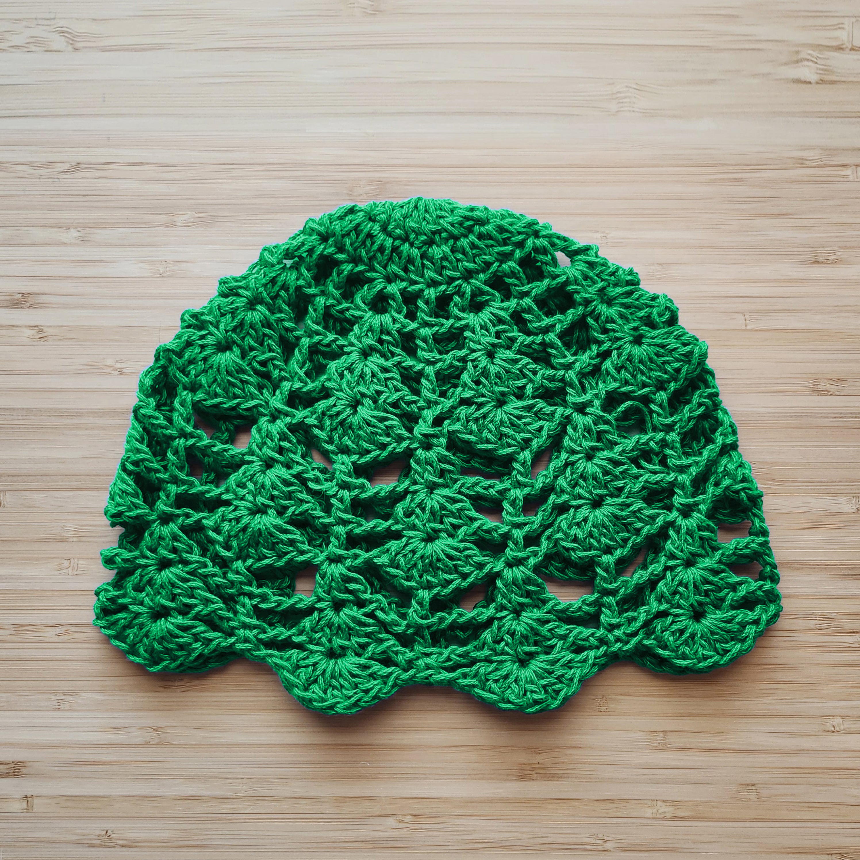 Green crocheted floral lace hat on a wooden surface.