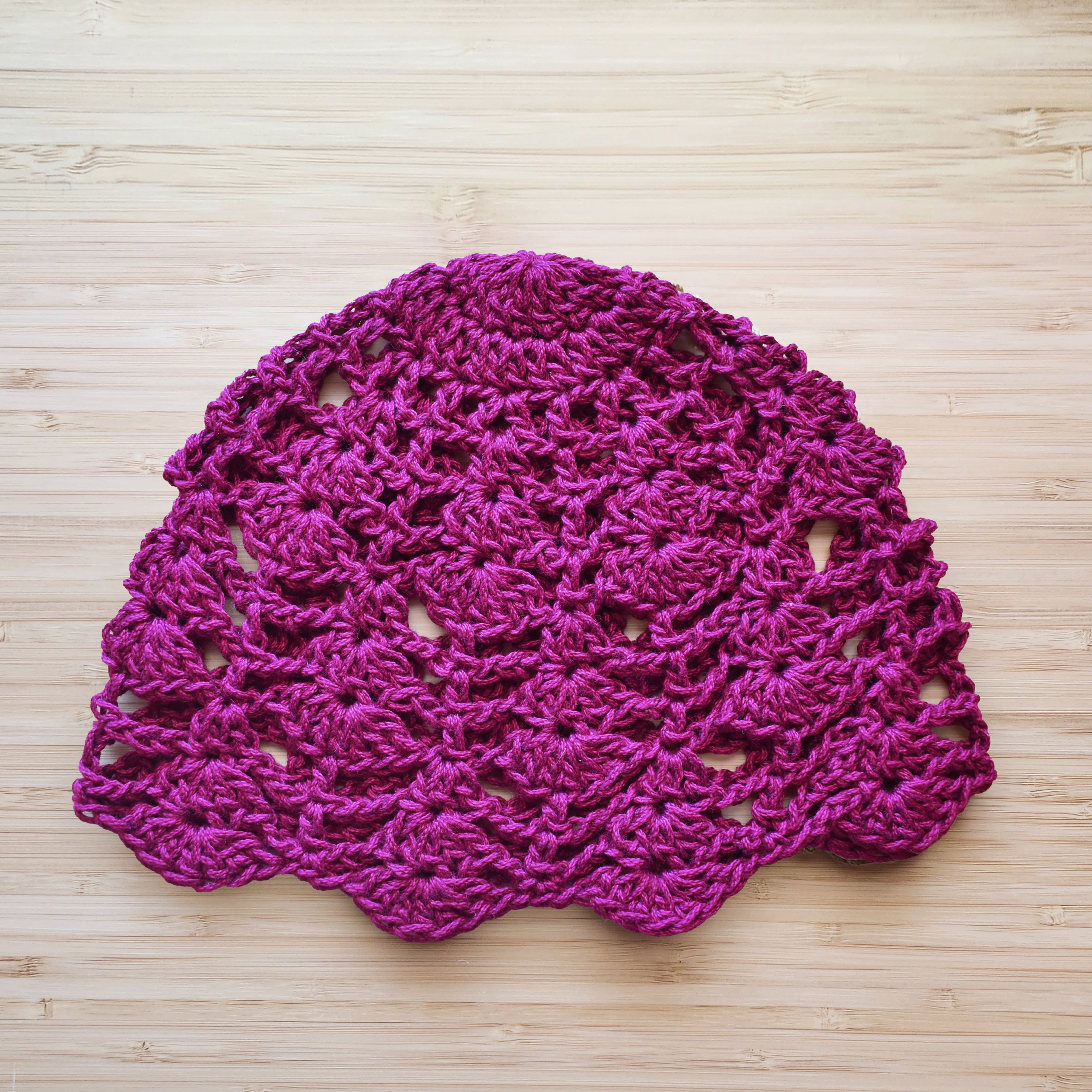 Magenta pink crocheted lace hat on a wooden surface.