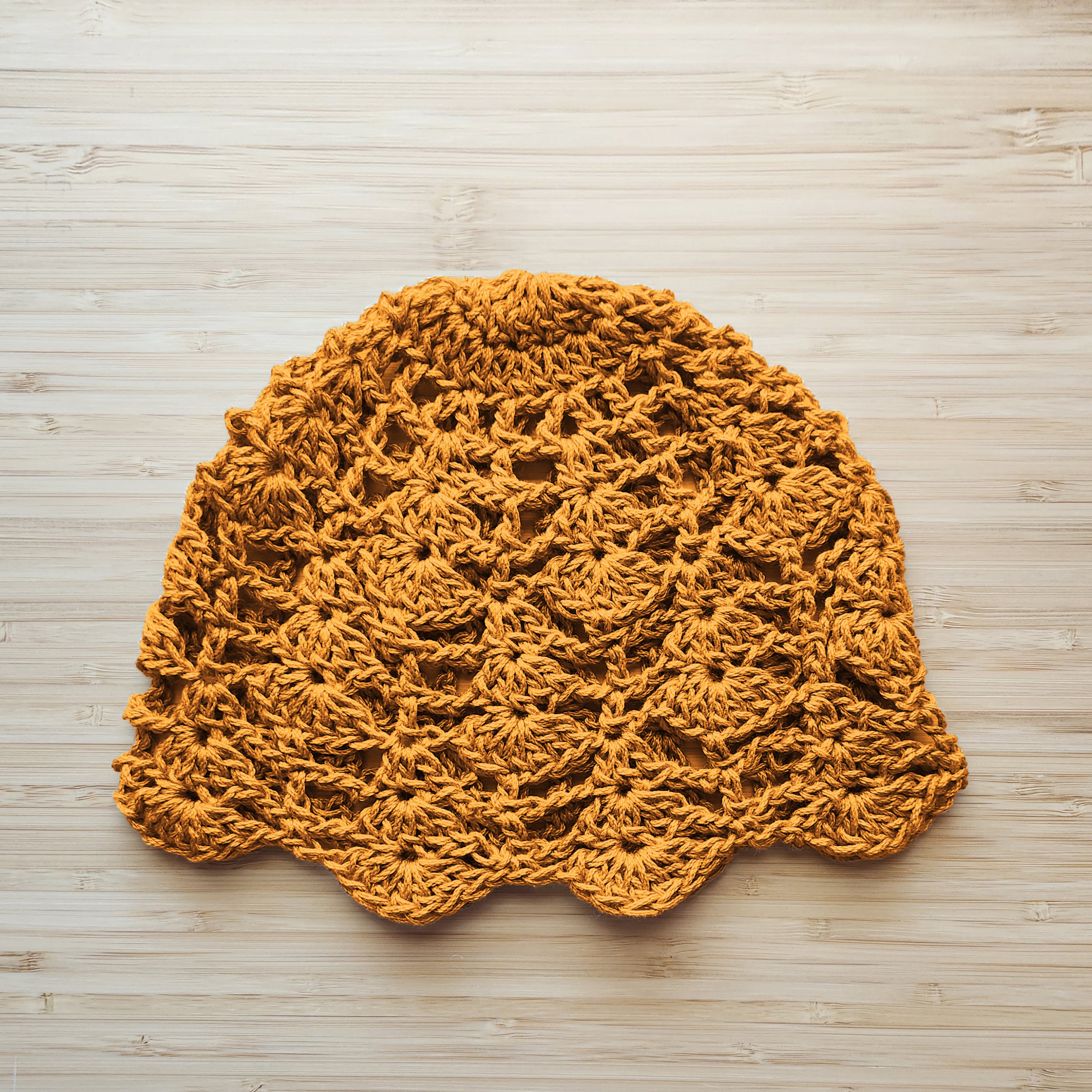 Crocheted yellow lace cap on a wooden surface.