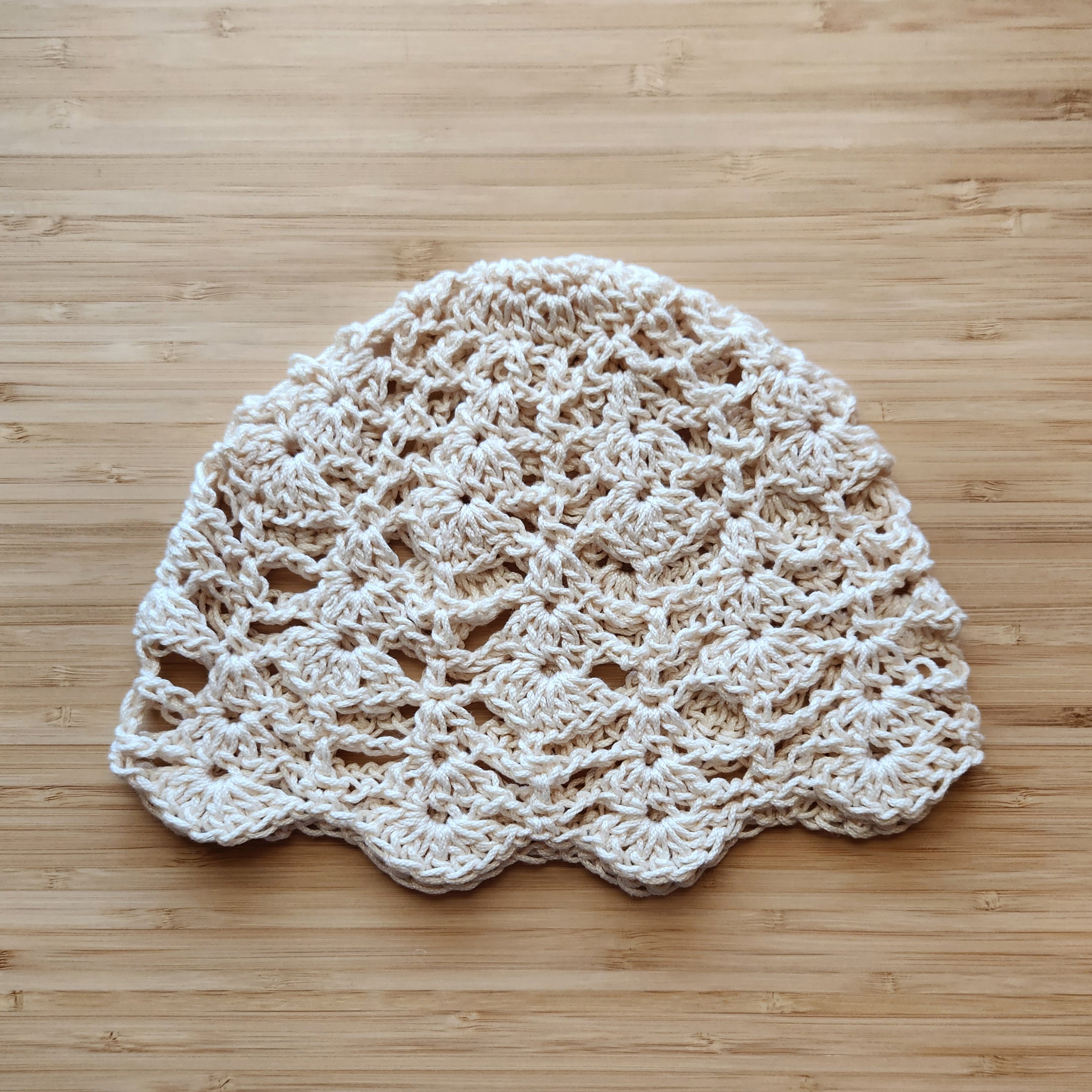 Crocheted beige hat with a floral pattern on a wooden surface.