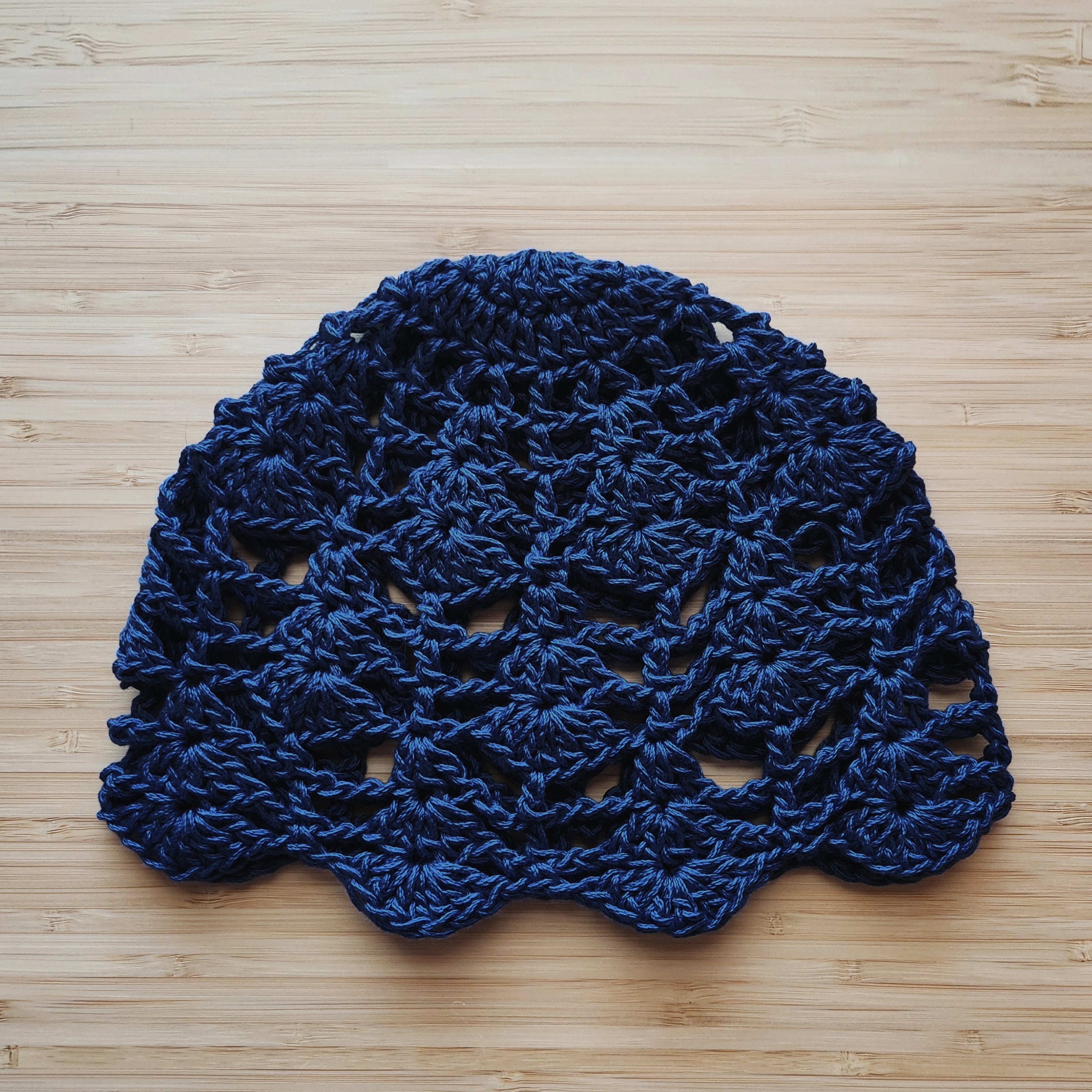 Navy blue crocheted boho lace skull cap on a wooden surface.