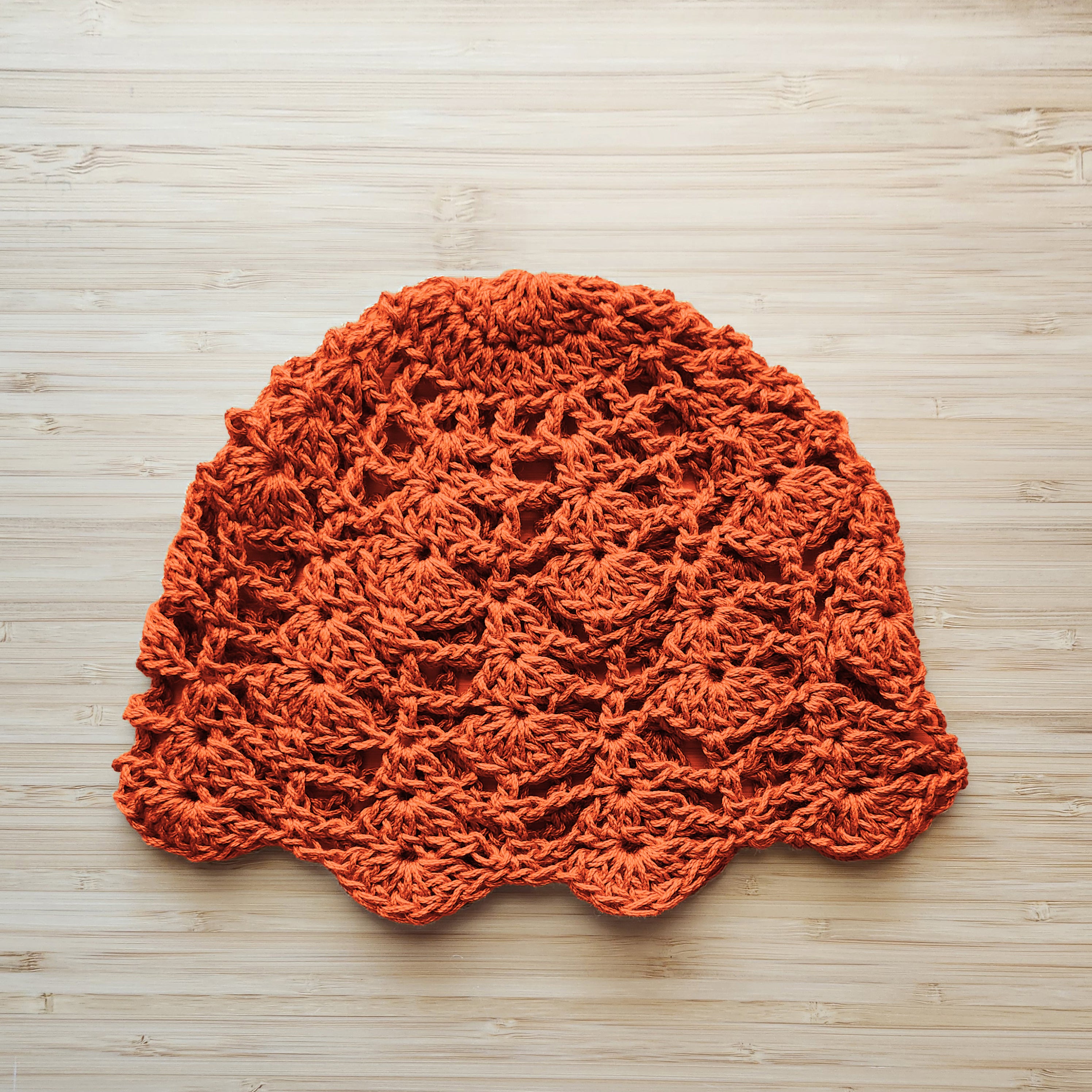 Orange crocheted lace cap on a wooden surface.