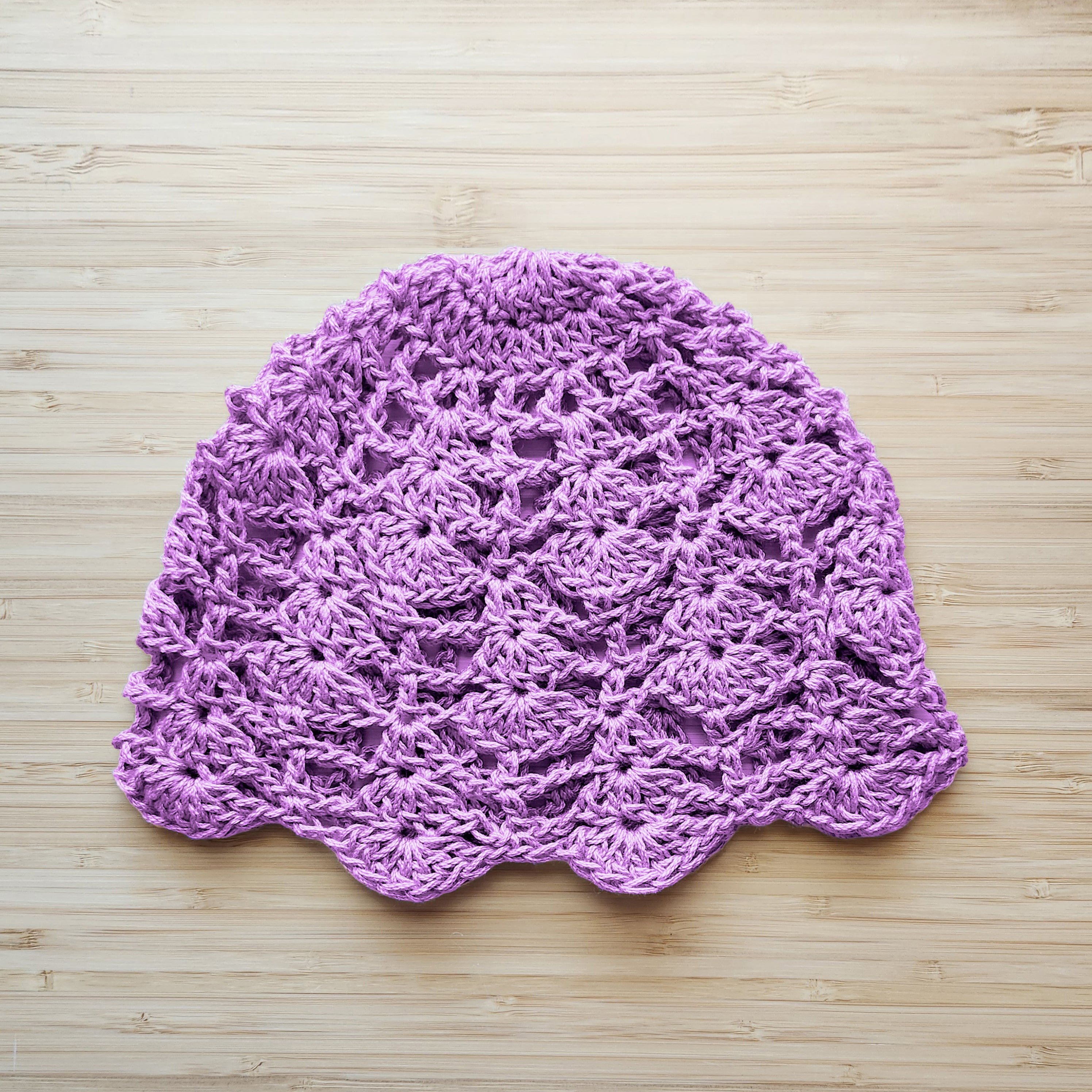 Light purple crocheted hat on a wooden surface.