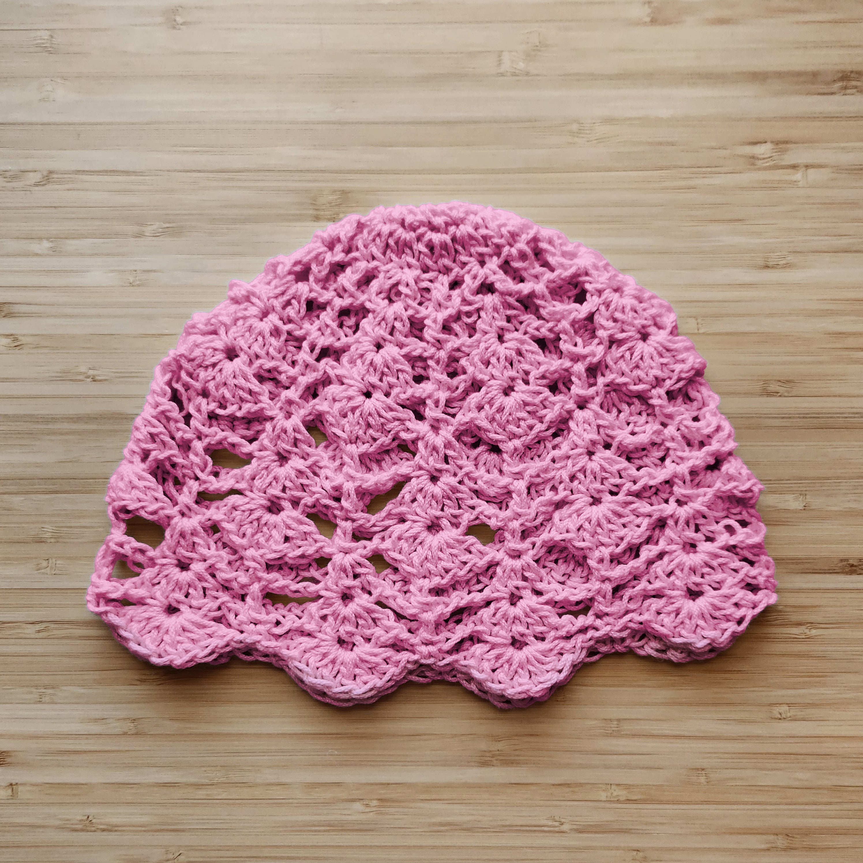 Pink crocheted lace skull cap on a wooden surface.