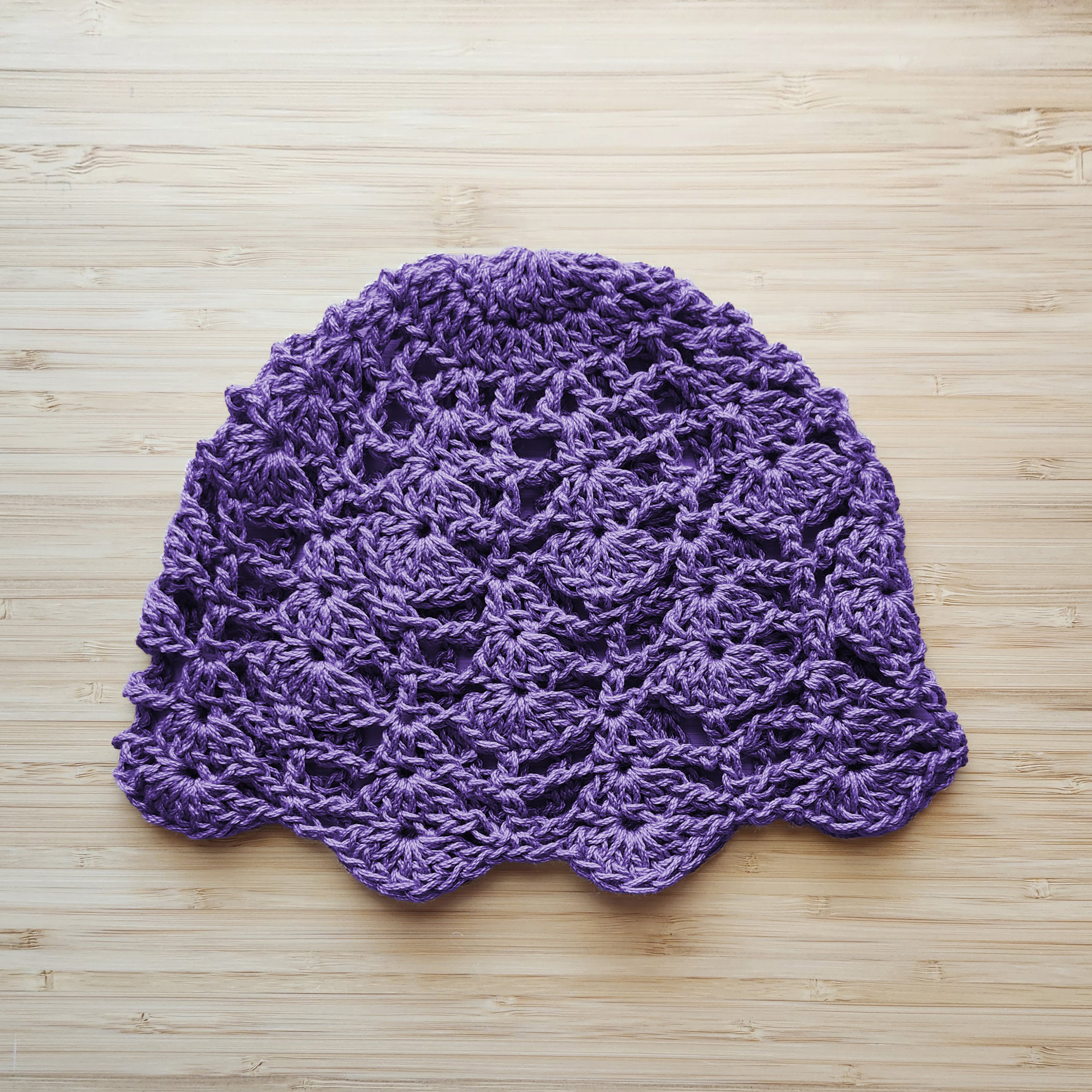 Purple crocheted hat with a floral lace design on a wooden surface.