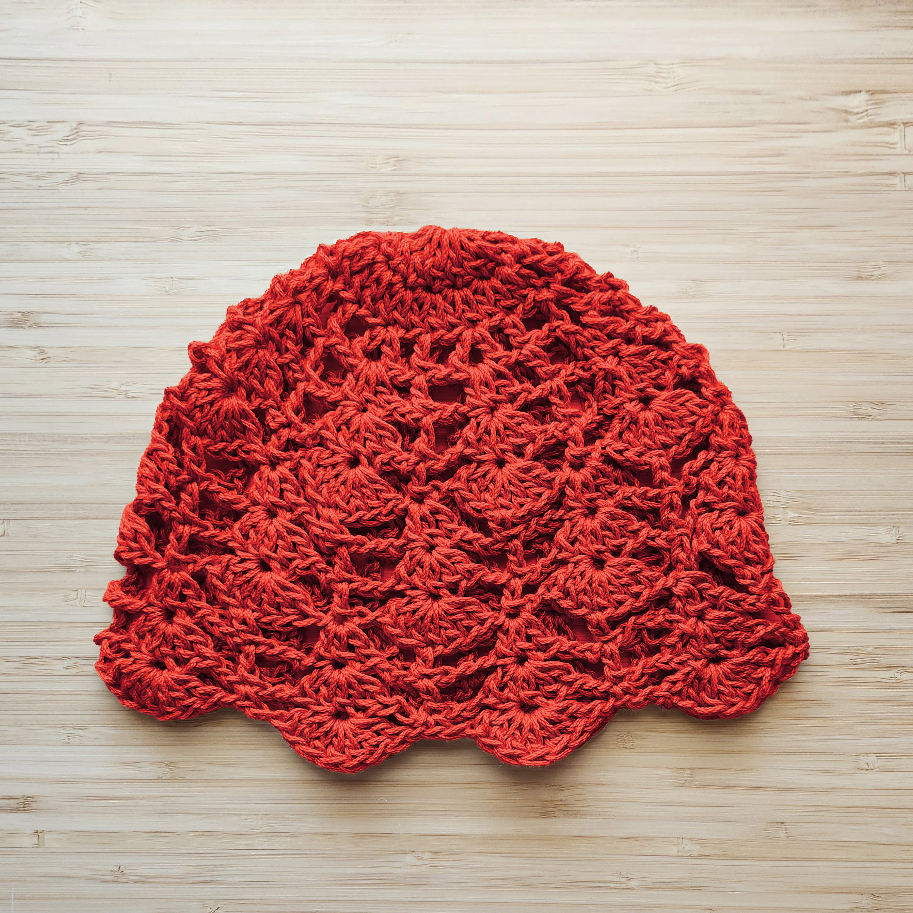 Red crocheted lace hat on a wooden surface.
