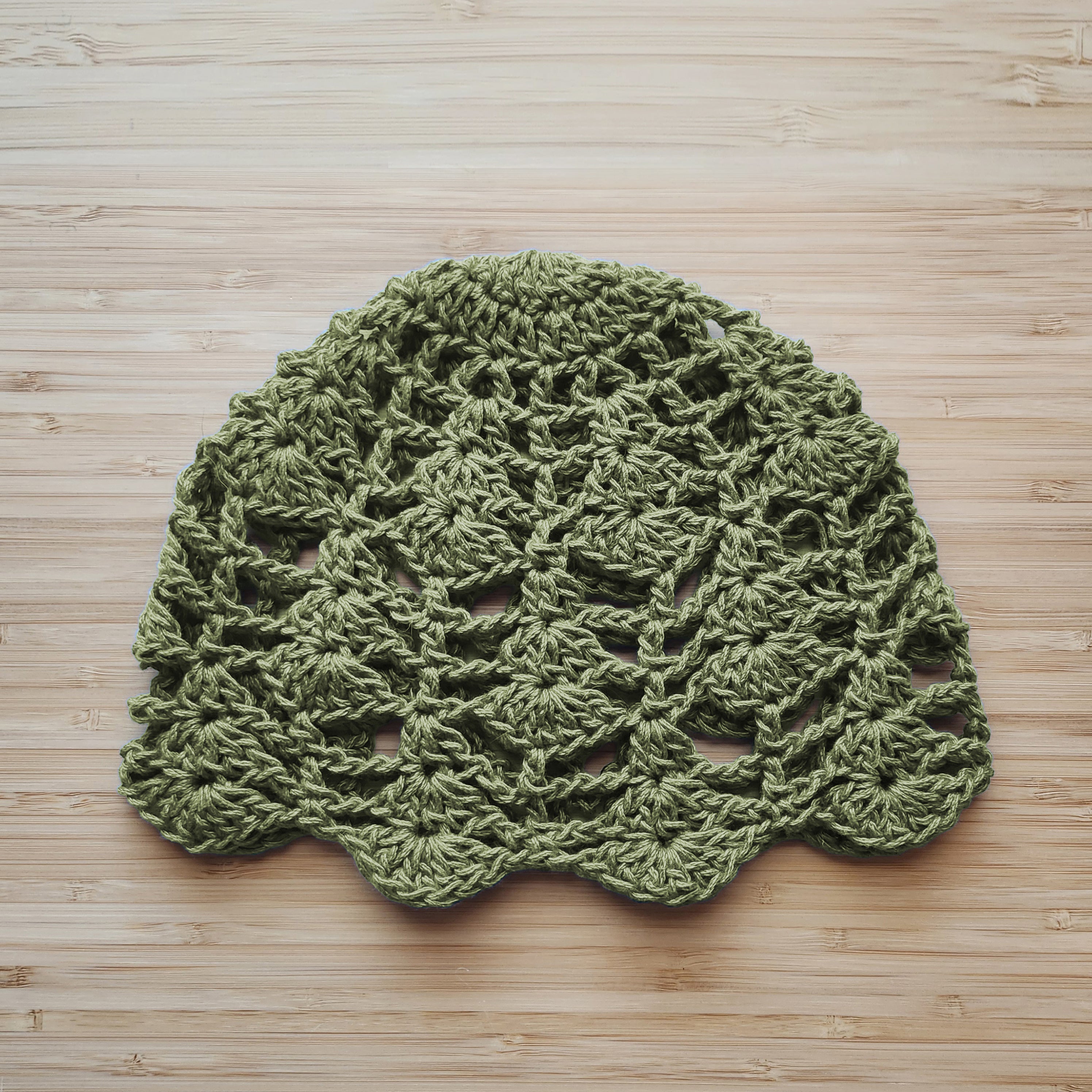 Sage green handmade crocheted lace hat on a wooden surface.