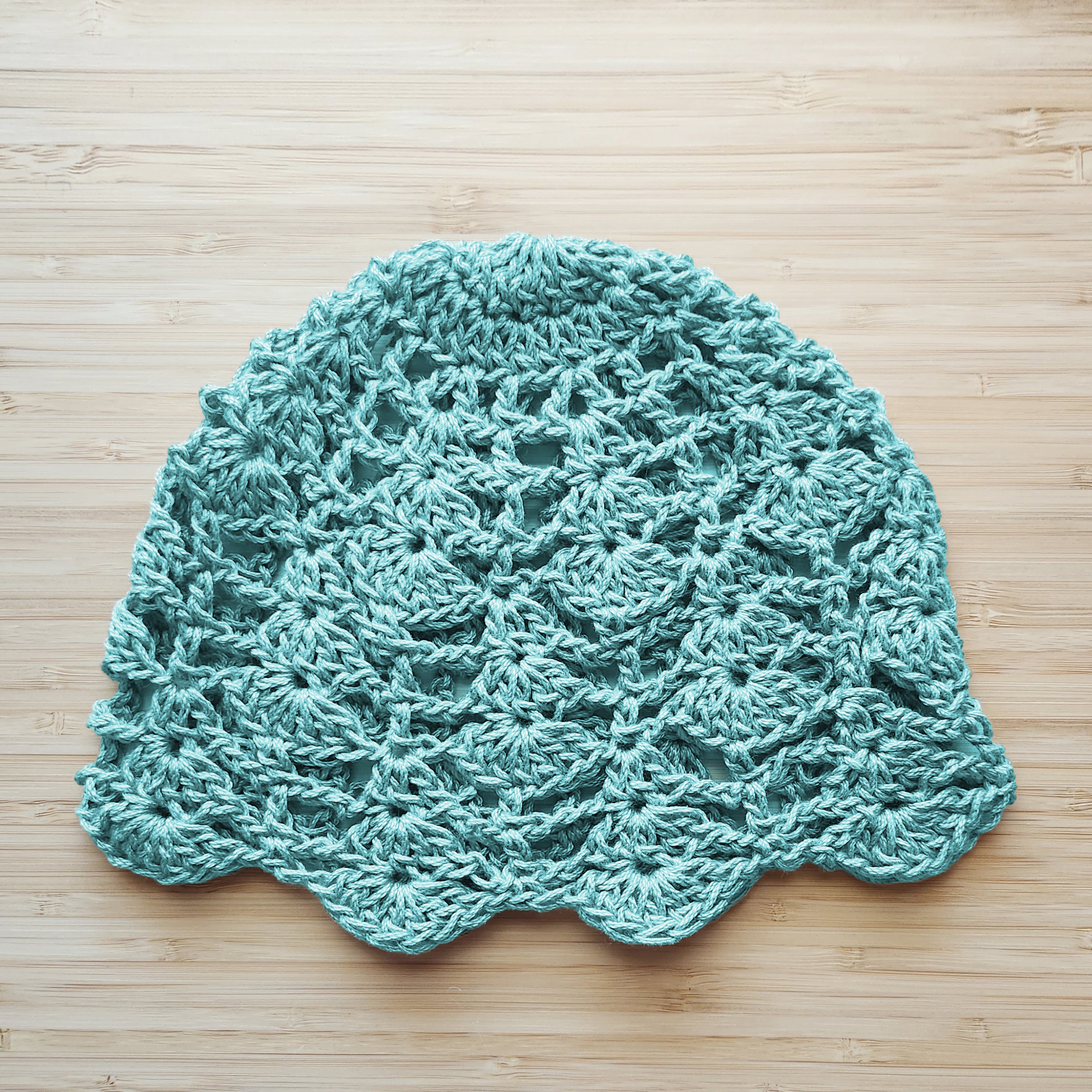 Turquoise crocheted floral lace hat on a wooden surface.