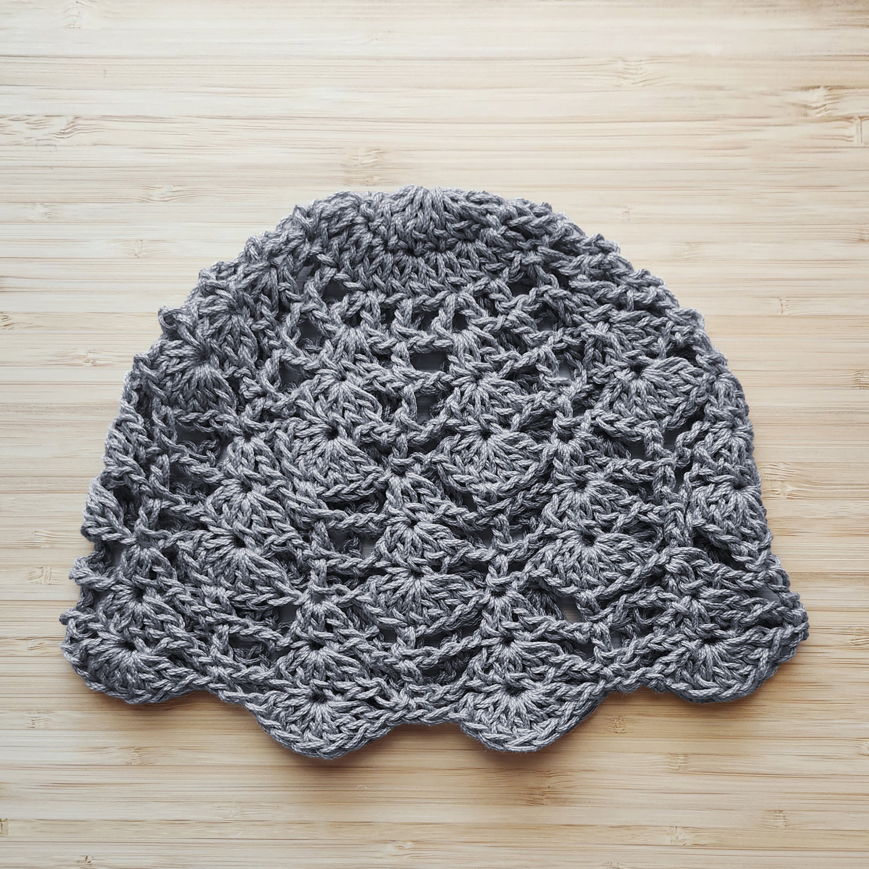 Gray crocheted lace hat on a wooden surface.