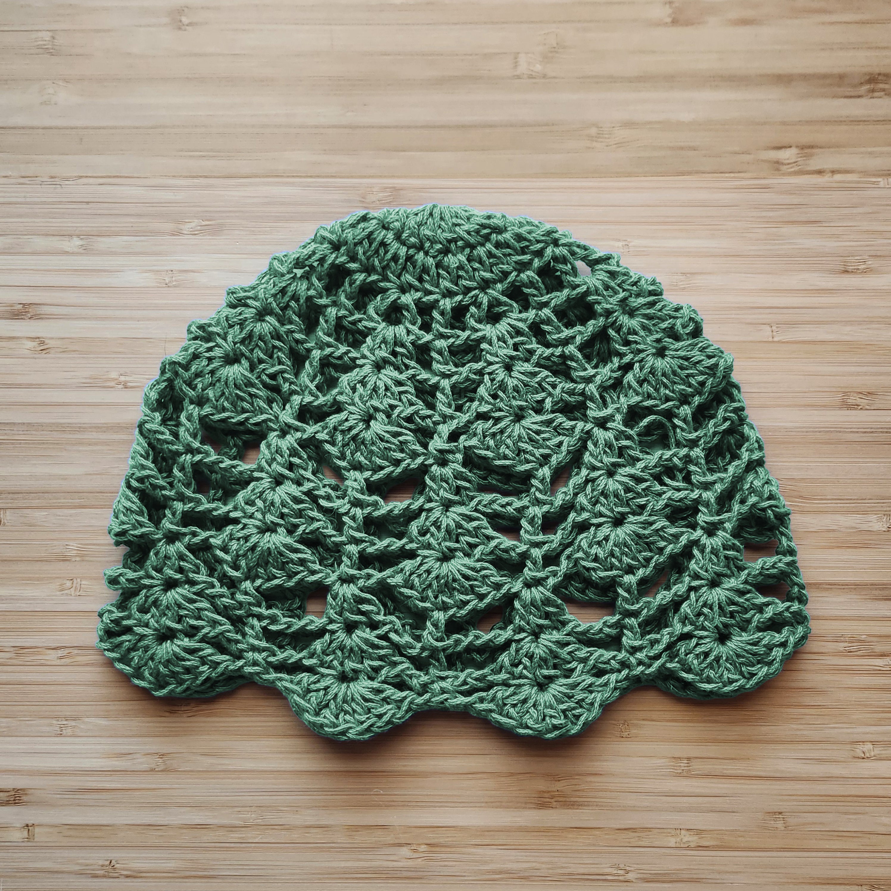 Green crocheted boho lace hat on a wooden surface.